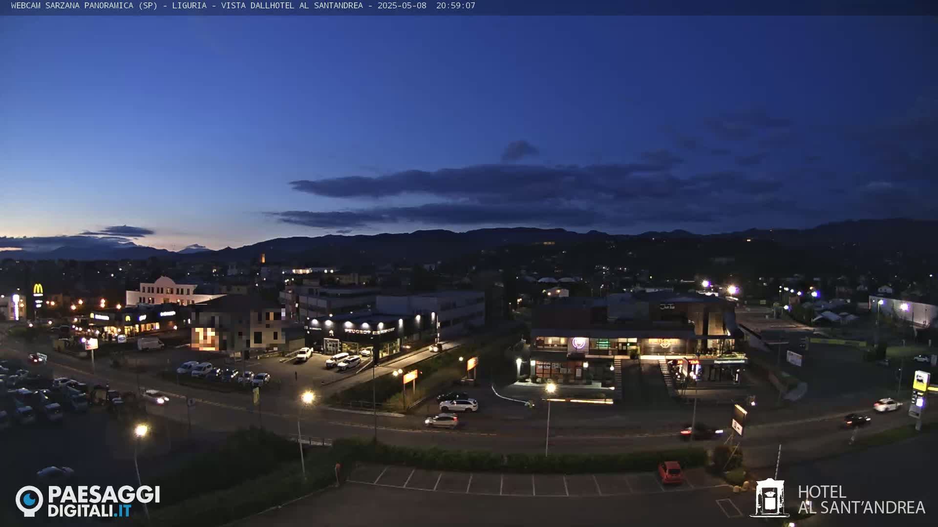 A nighttime, high-angle view of a town nestled in a valley, under a mostly clear, dark blue twilight sky.