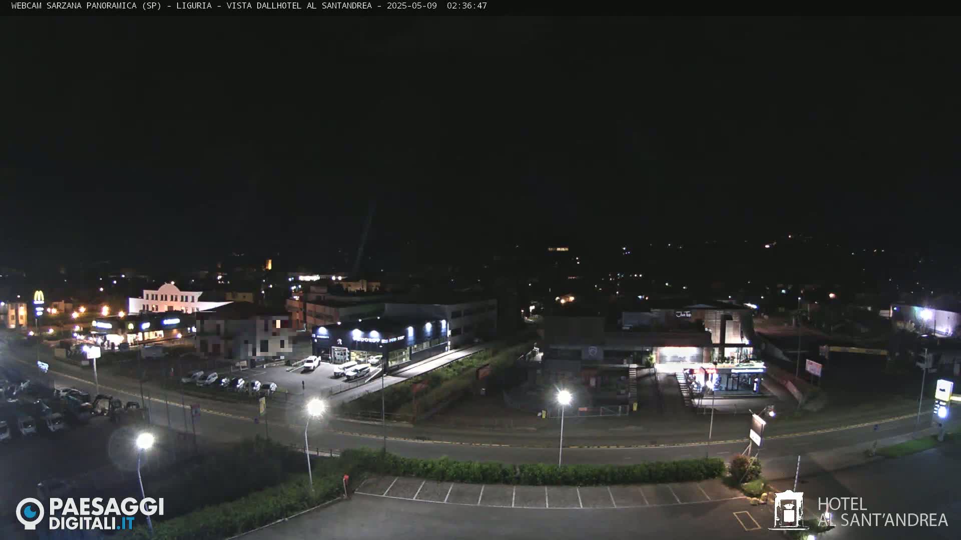 A nighttime, aerial view of a town's illuminated streets, buildings, and parking lots.