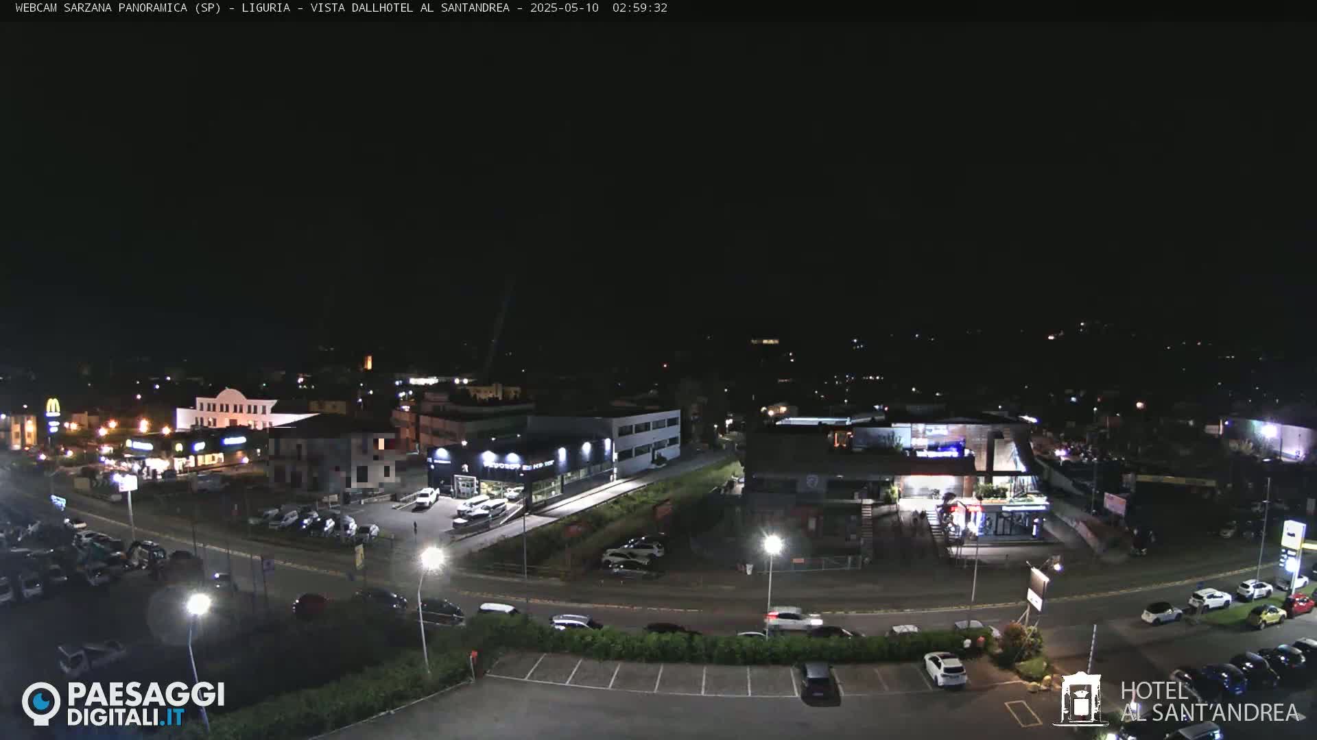 A nighttime aerial view of a town’s parking lots and buildings, illuminated by streetlights.