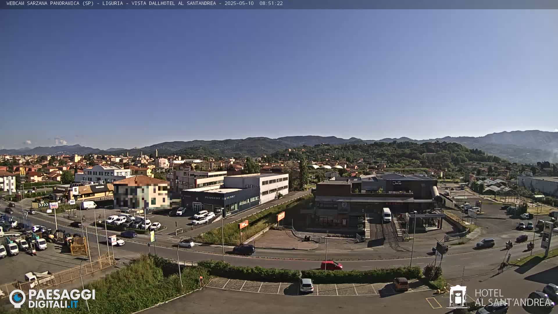 A sunny, clear day overlooks a town with buildings, roads, and cars, backed by distant mountains.