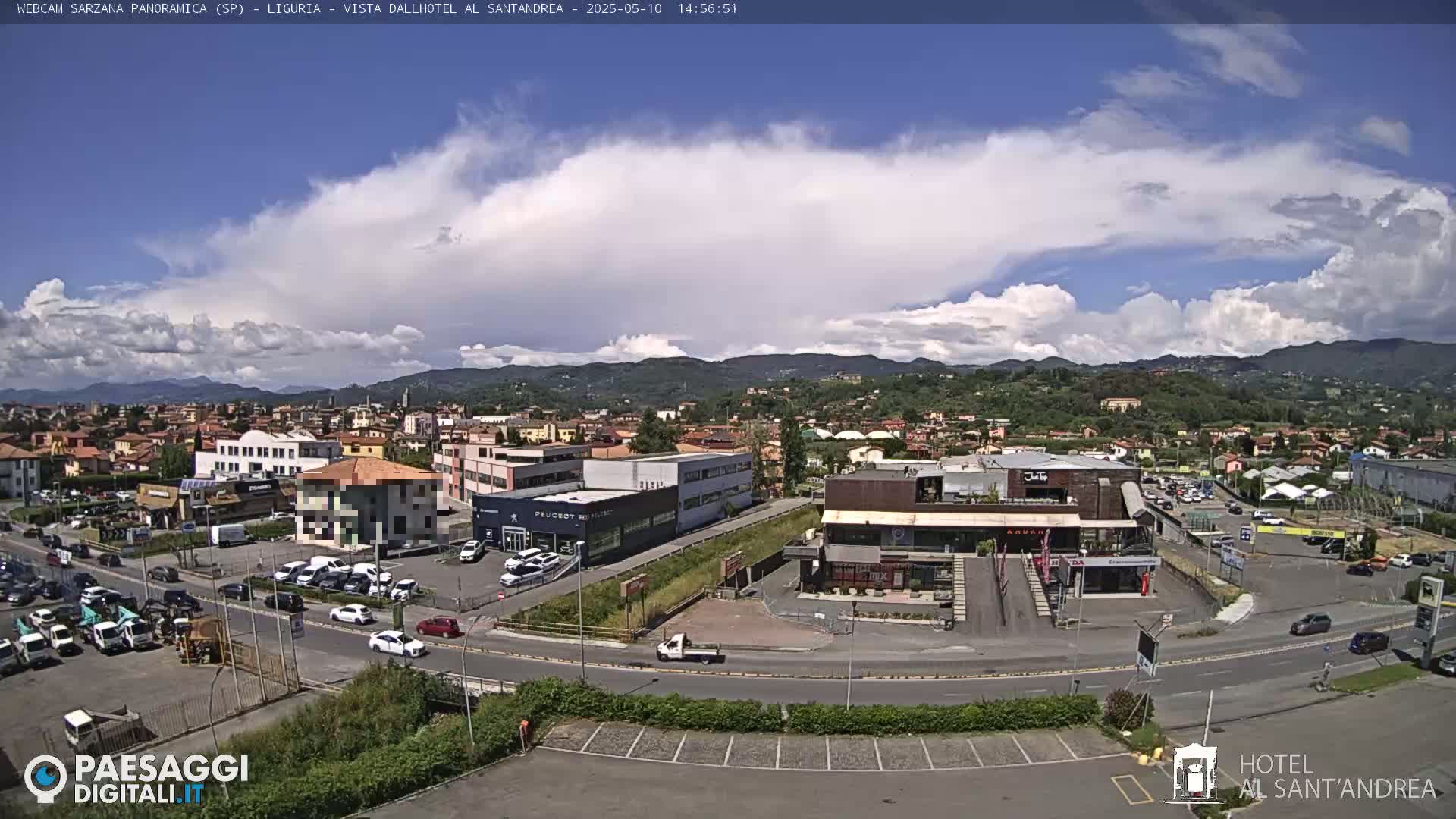 A partly cloudy day reveals a sprawling town nestled in a valley, surrounded by verdant hills and mountains.