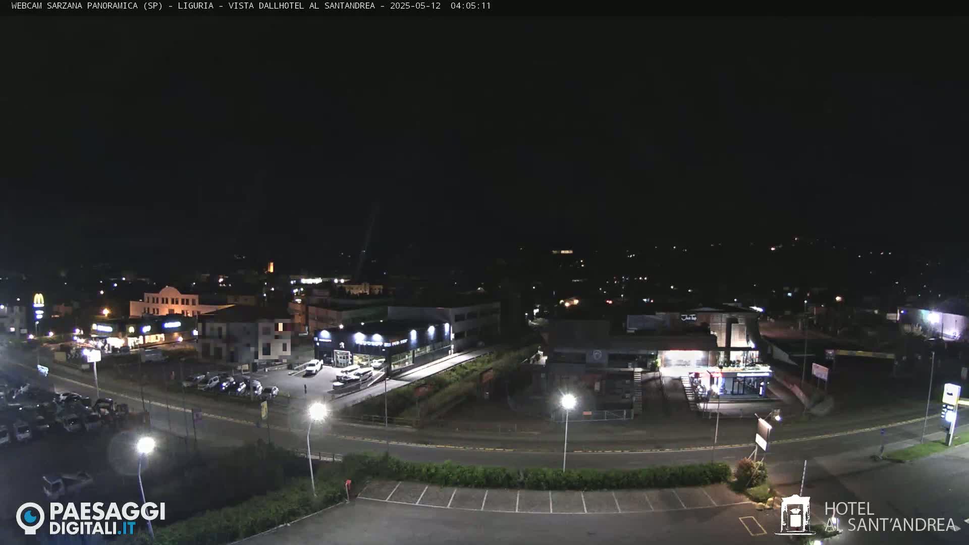 A nighttime aerial view of a town with illuminated buildings and roads, and cars parked in lots.