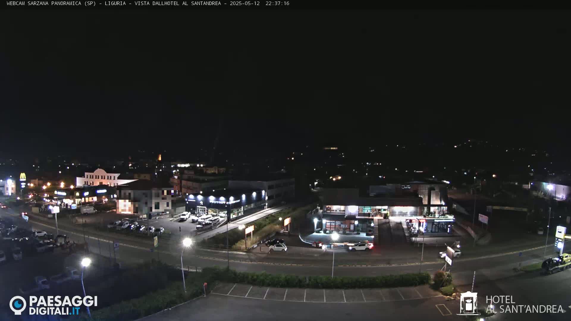 A nighttime, aerial view of a highway intersection and surrounding businesses, including parking lots and buildings with illuminated signs.