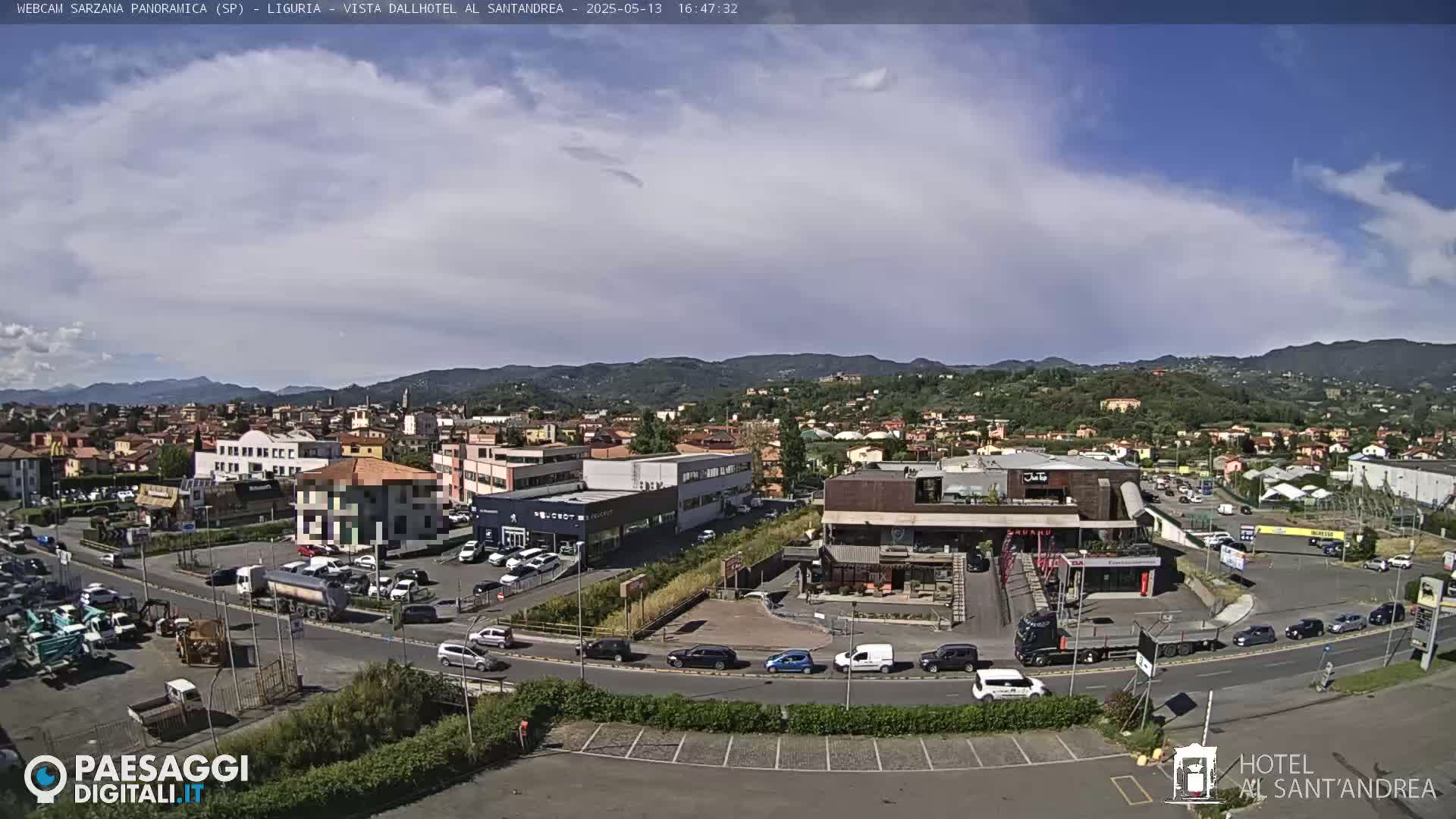 A panoramic view of a town under partly cloudy skies shows a parking lot, roads, buildings, and distant hills.