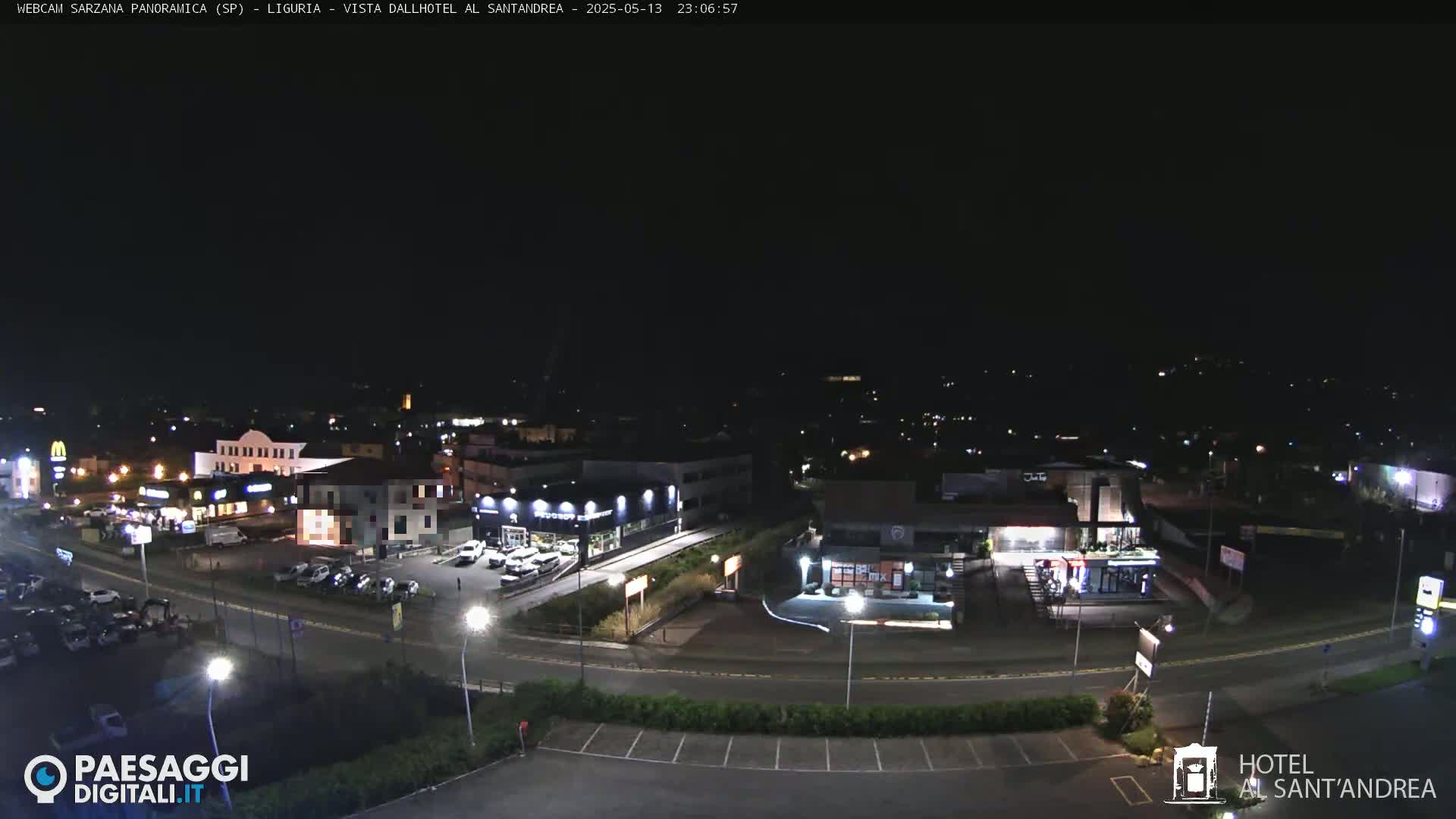 A nighttime, aerial view of a town's street scene with illuminated buildings and parked cars.