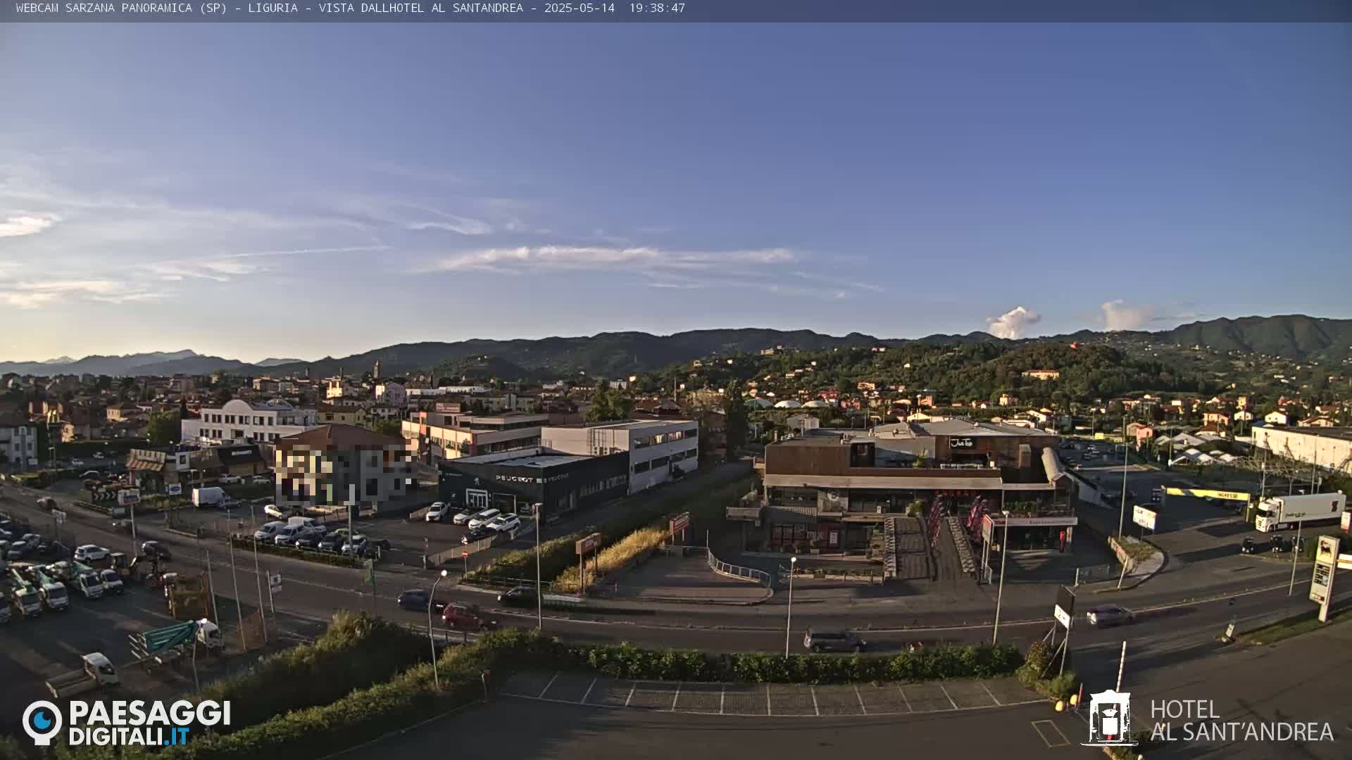 A clear, late afternoon view of a town nestled in a valley, with mountains in the background and numerous cars in a parking lot and on roads.
