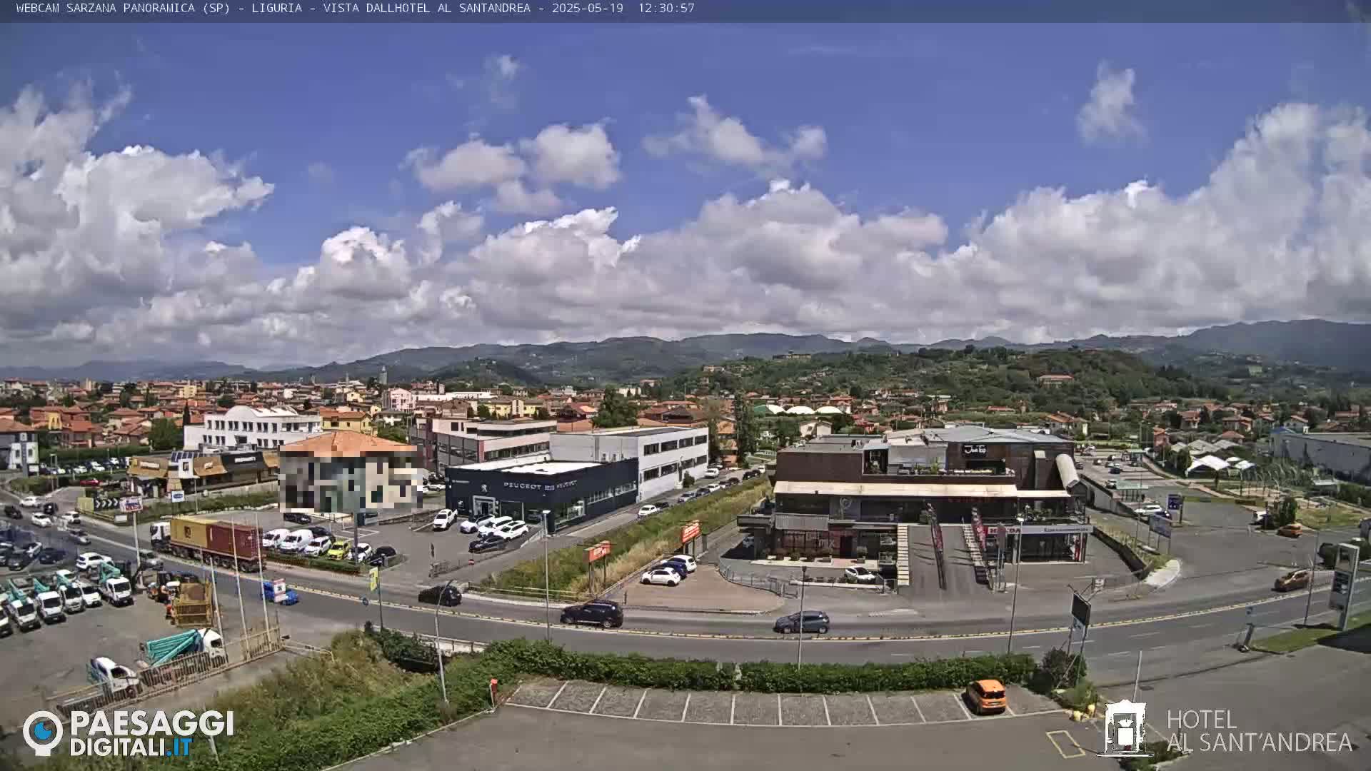 A partly cloudy day reveals a panoramic view of a town nestled amongst rolling hills, with a roadway curving through a parking lot filled with cars and trucks.