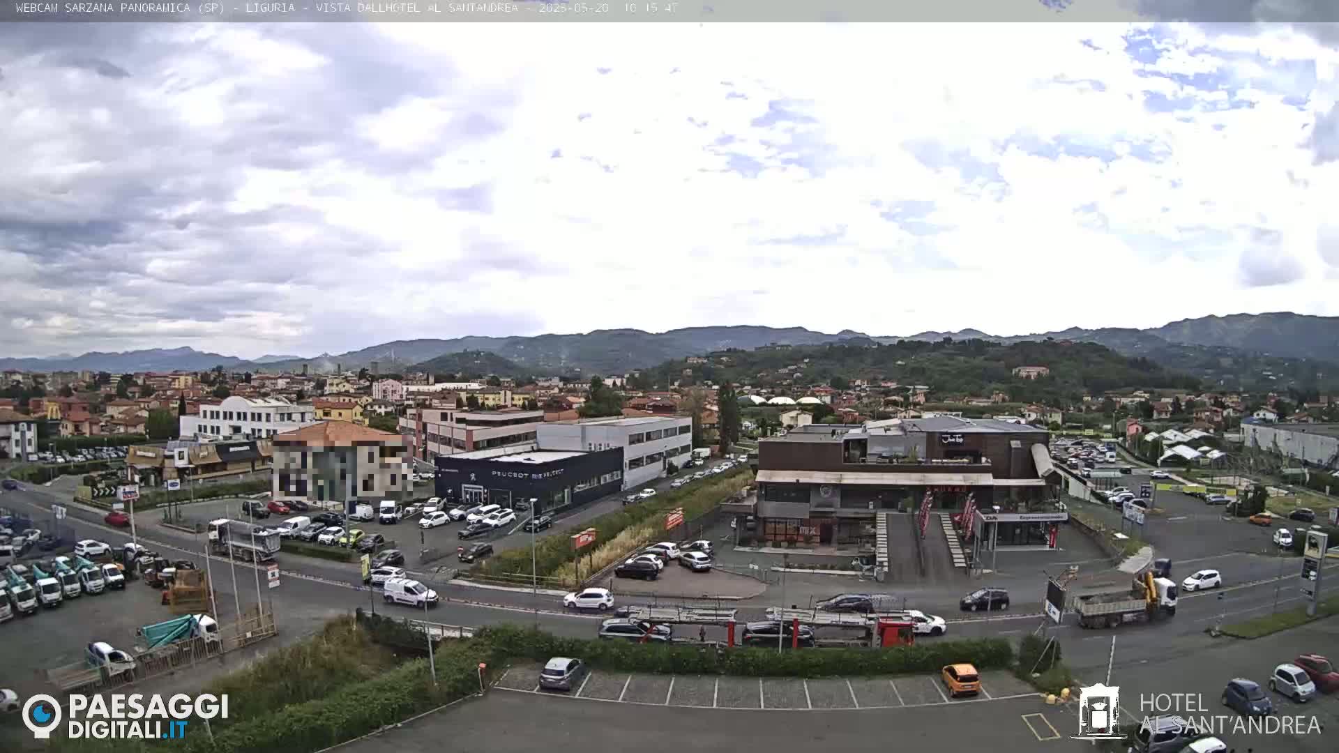 A partly cloudy day reveals a panoramic view of a town nestled in a valley surrounded by mountains, with numerous cars parked in lots near various buildings and businesses.