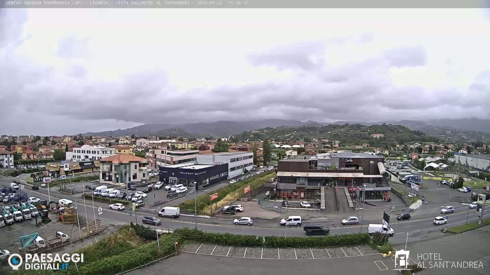 A cloudy day reveals a panoramic view of a town nestled amidst rolling hills, with various buildings, parked cars, and roads visible in the foreground.