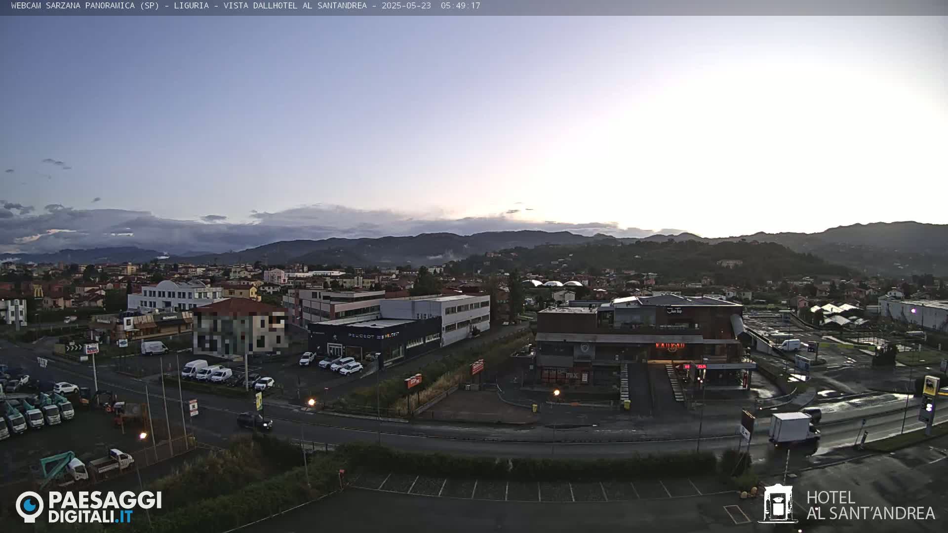A panoramic view of a town nestled in a valley at dawn, under a mostly clear sky with some clouds.