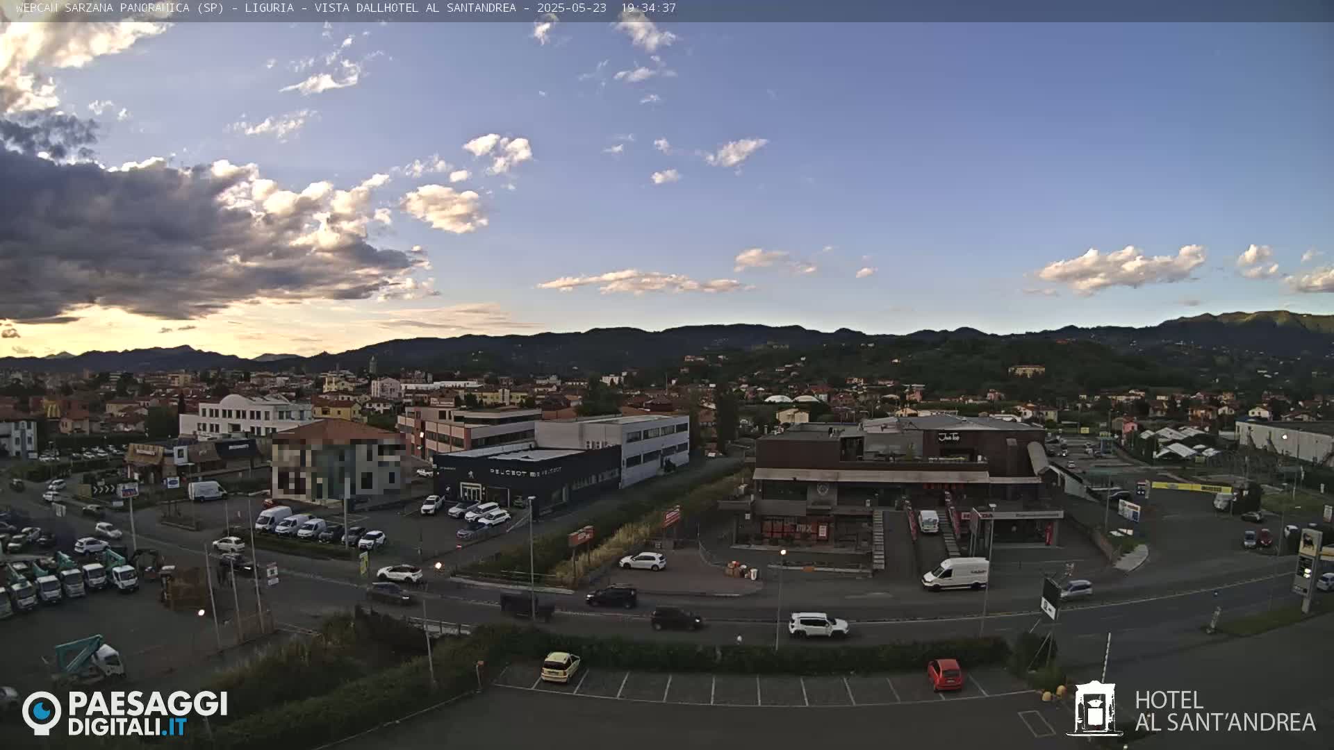 A partly cloudy sunset over a town with numerous buildings and cars in a parking lot.