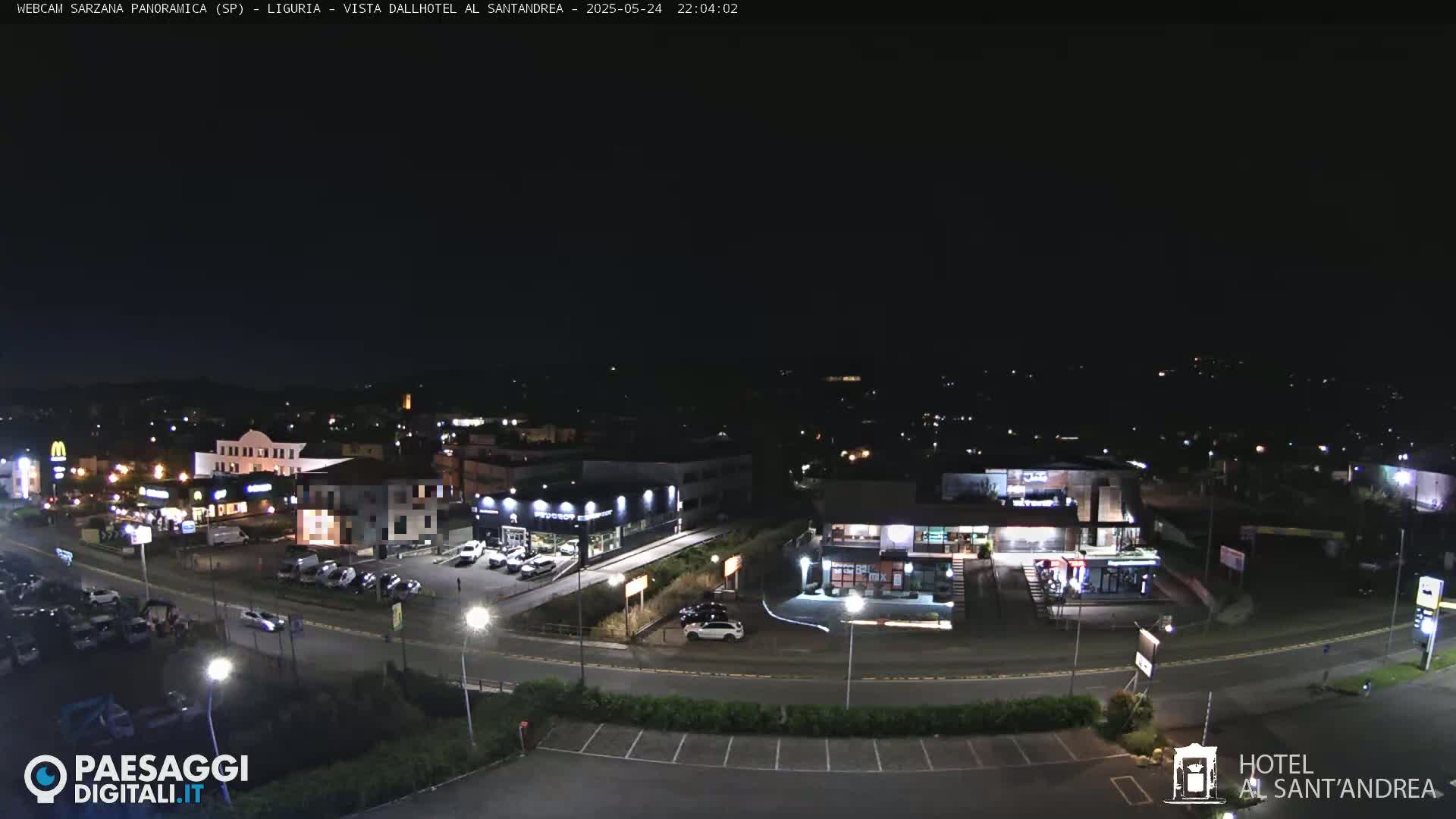 A nighttime aerial view of a town with several buildings, parking lots, and roadways, under a clear, dark sky.