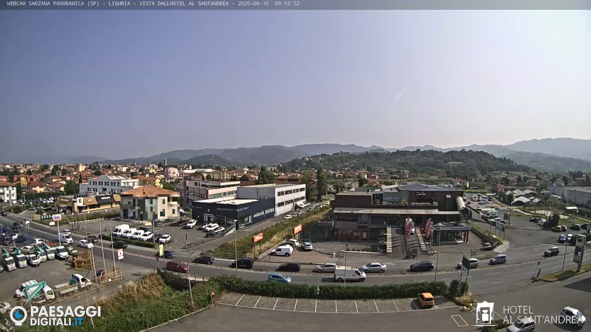 A sunny, clear day reveals a sprawling town with various buildings, cars in parking lots and on roads, and a mountain range in the background.