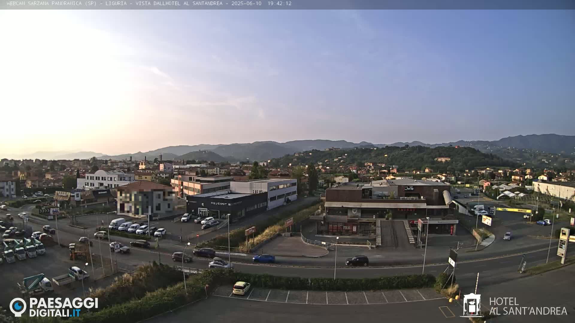 A clear, dusk-lit view of a town in a valley, showing buildings, roads, cars, and distant hills.