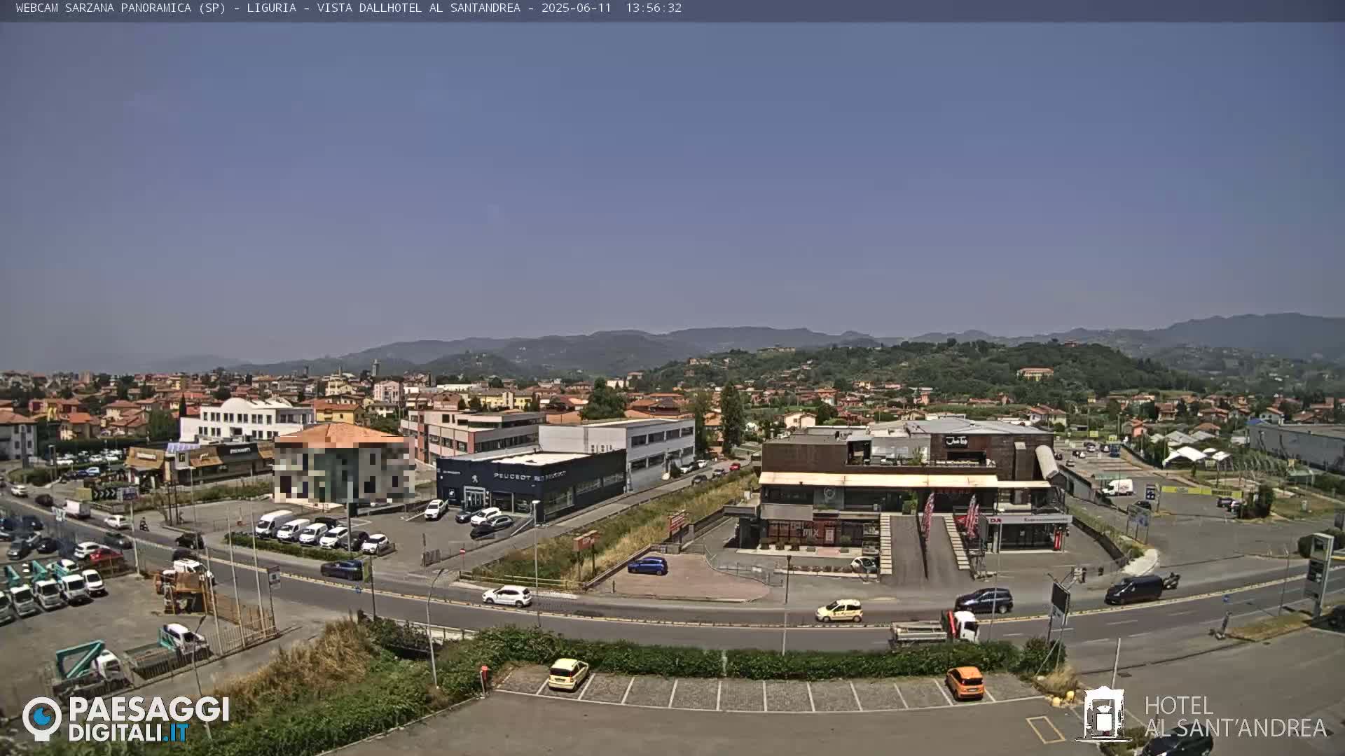 A clear, sunny day reveals a panoramic view of a town nestled among rolling hills, showcasing a mix of buildings, roads, and parked cars.