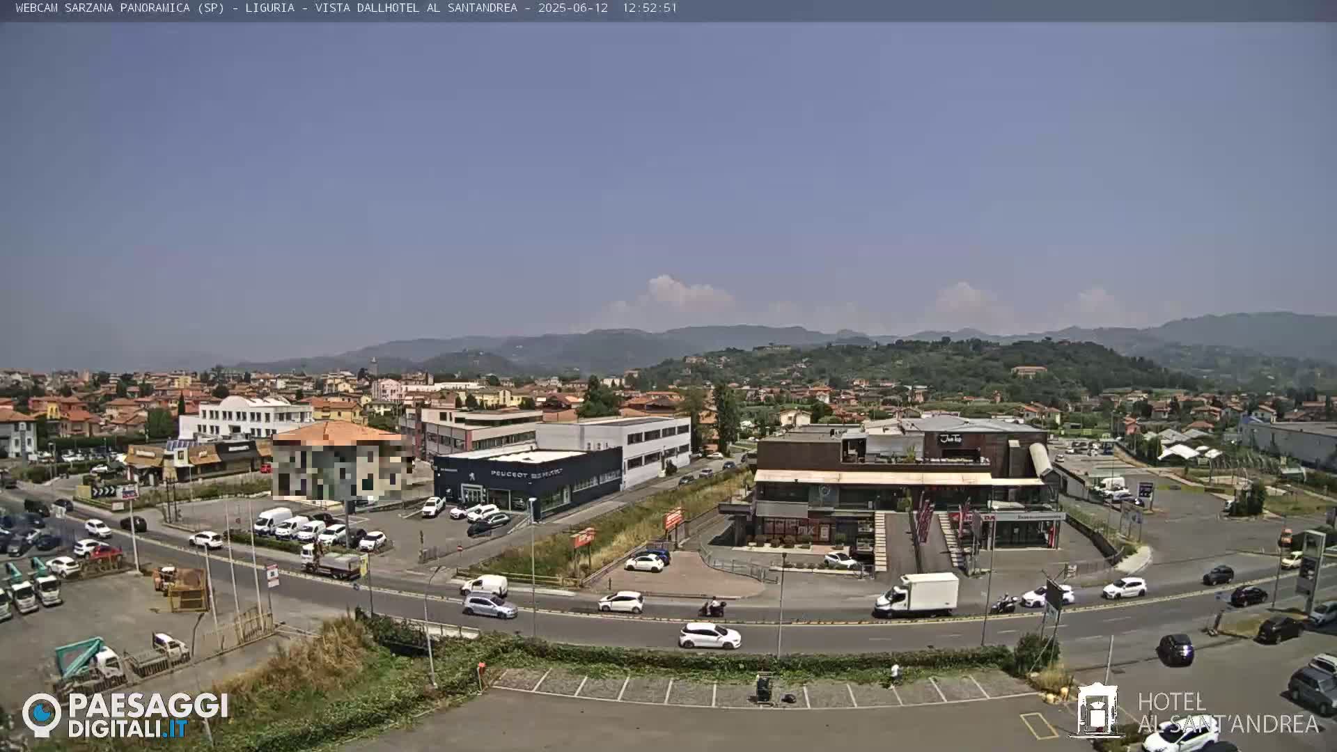 A sunny, high-angle view of a town featuring buildings, roads, cars, and a landscape of hills in the background.