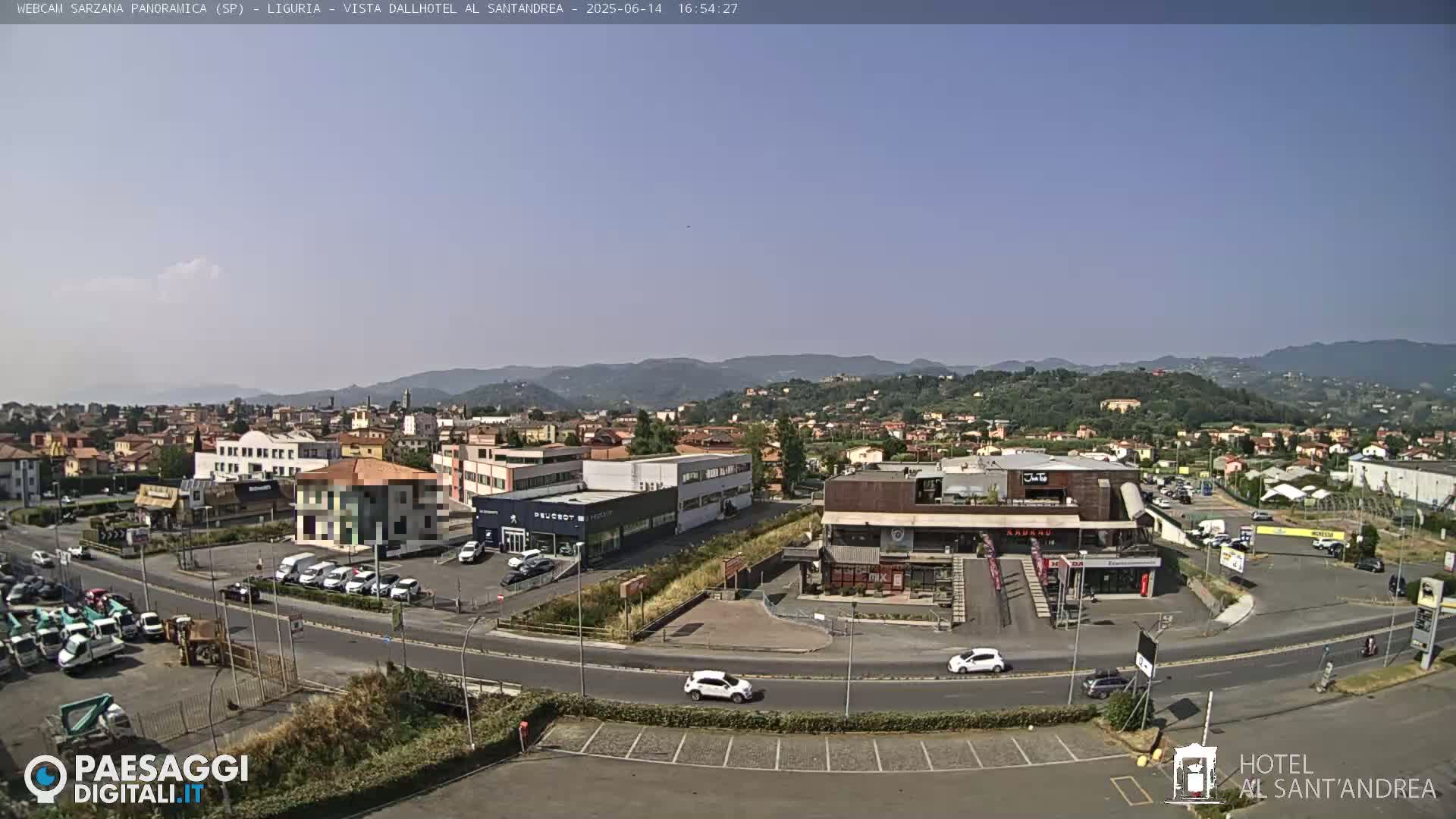 A clear, sunny day reveals a sprawling town vista, featuring buildings, roads, and parked cars, with distant hills under a light blue sky.