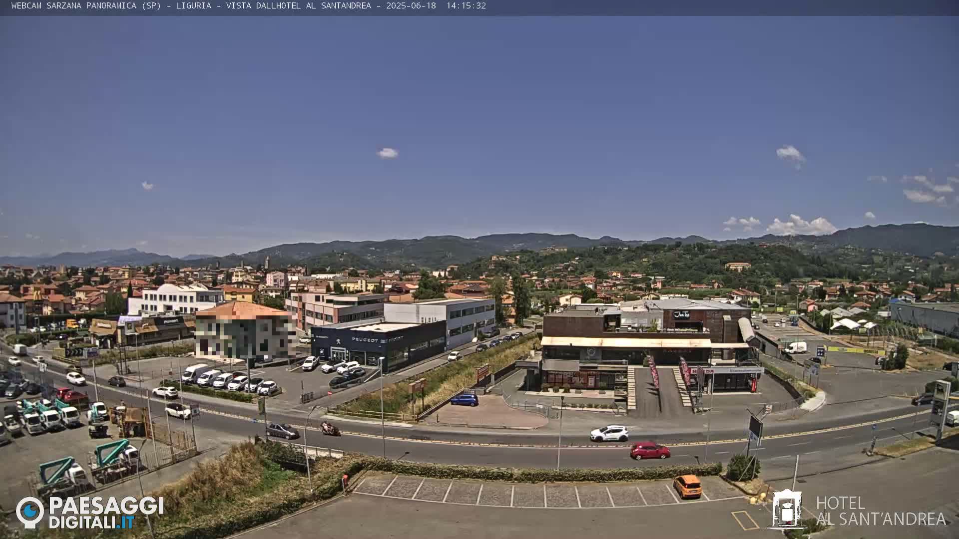A sunny, clear day overlooking a town with buildings, cars, and a car dealership, all set against a backdrop of distant hills.
