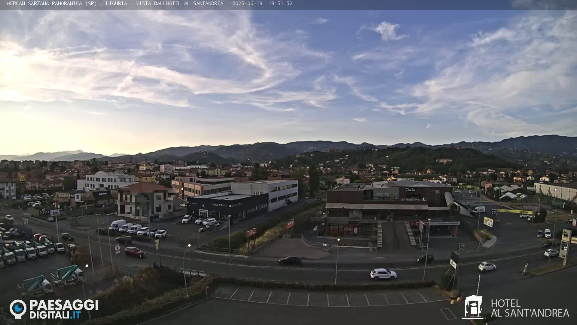 A partly cloudy evening scene overlooks a town nestled in a valley, with mountains in the distance.