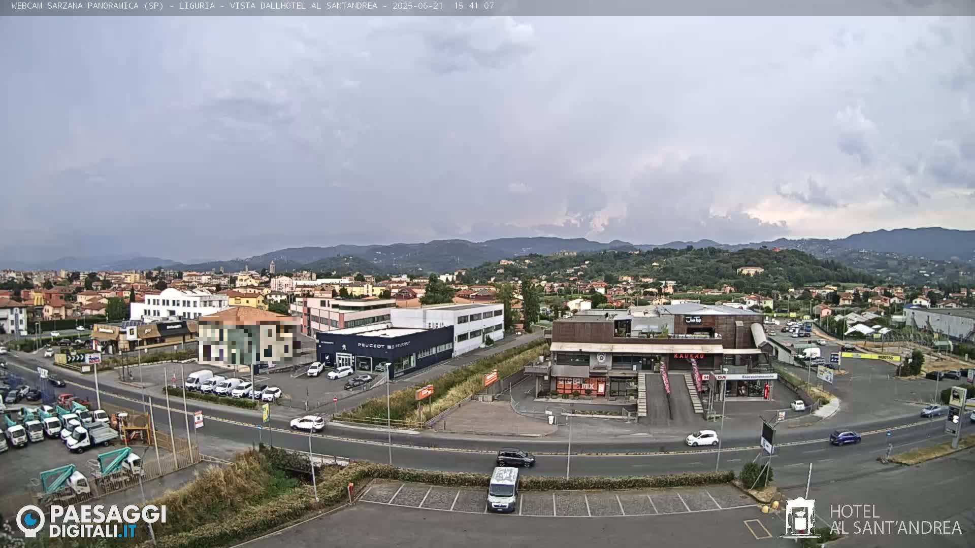 An overcast day reveals a view of a town nestled among hills, with various buildings, vehicles, and roads visible.