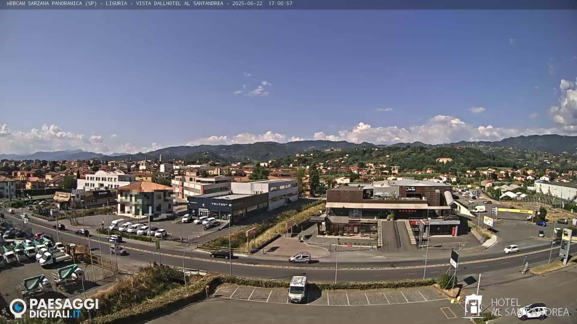 A sunny day reveals a town nestled in a valley, with cars parked in lots surrounding buildings and roads.