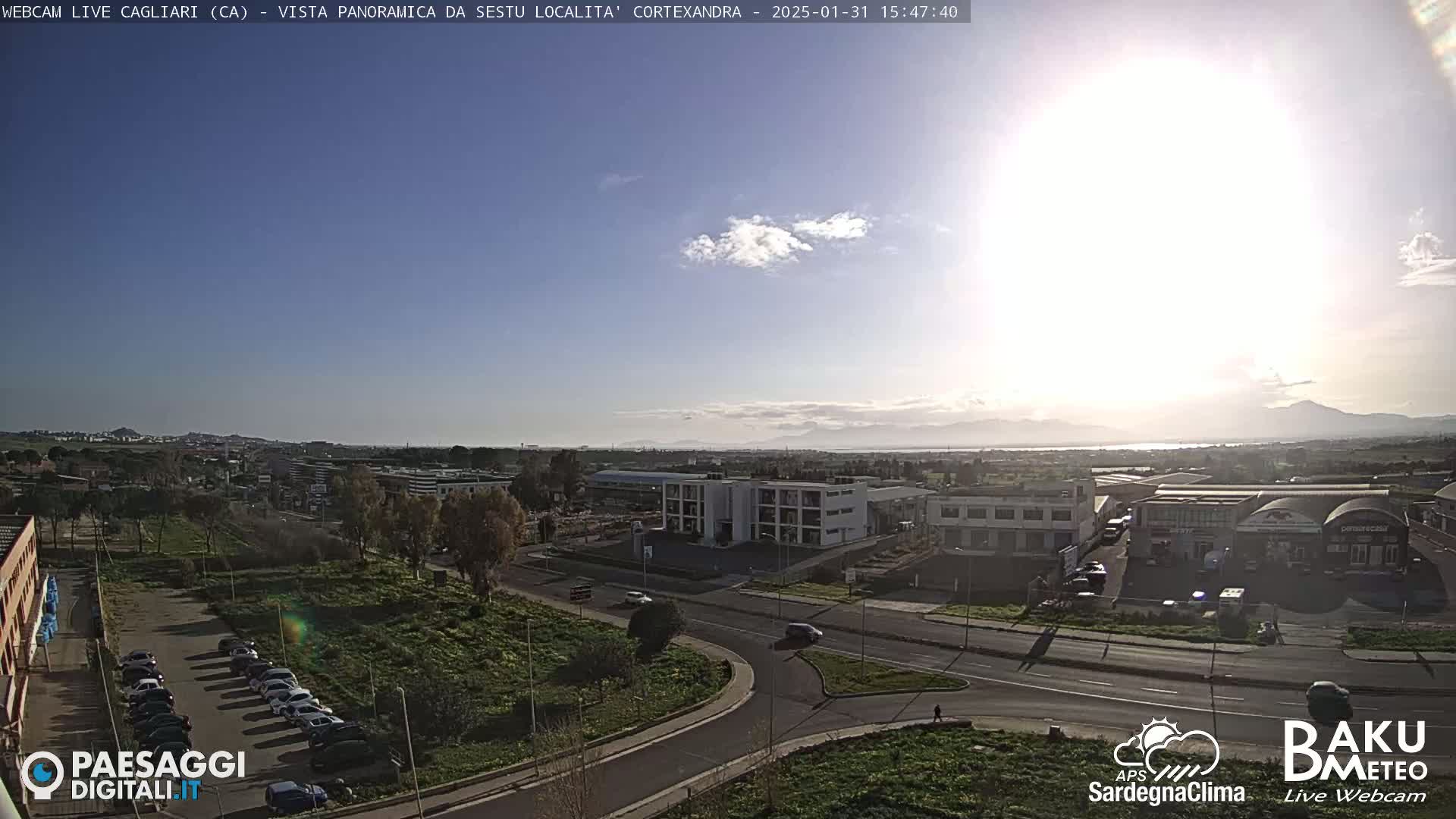 A sunny day reveals a panoramic view of an industrial area and a parking lot, with mountains visible in the distance.