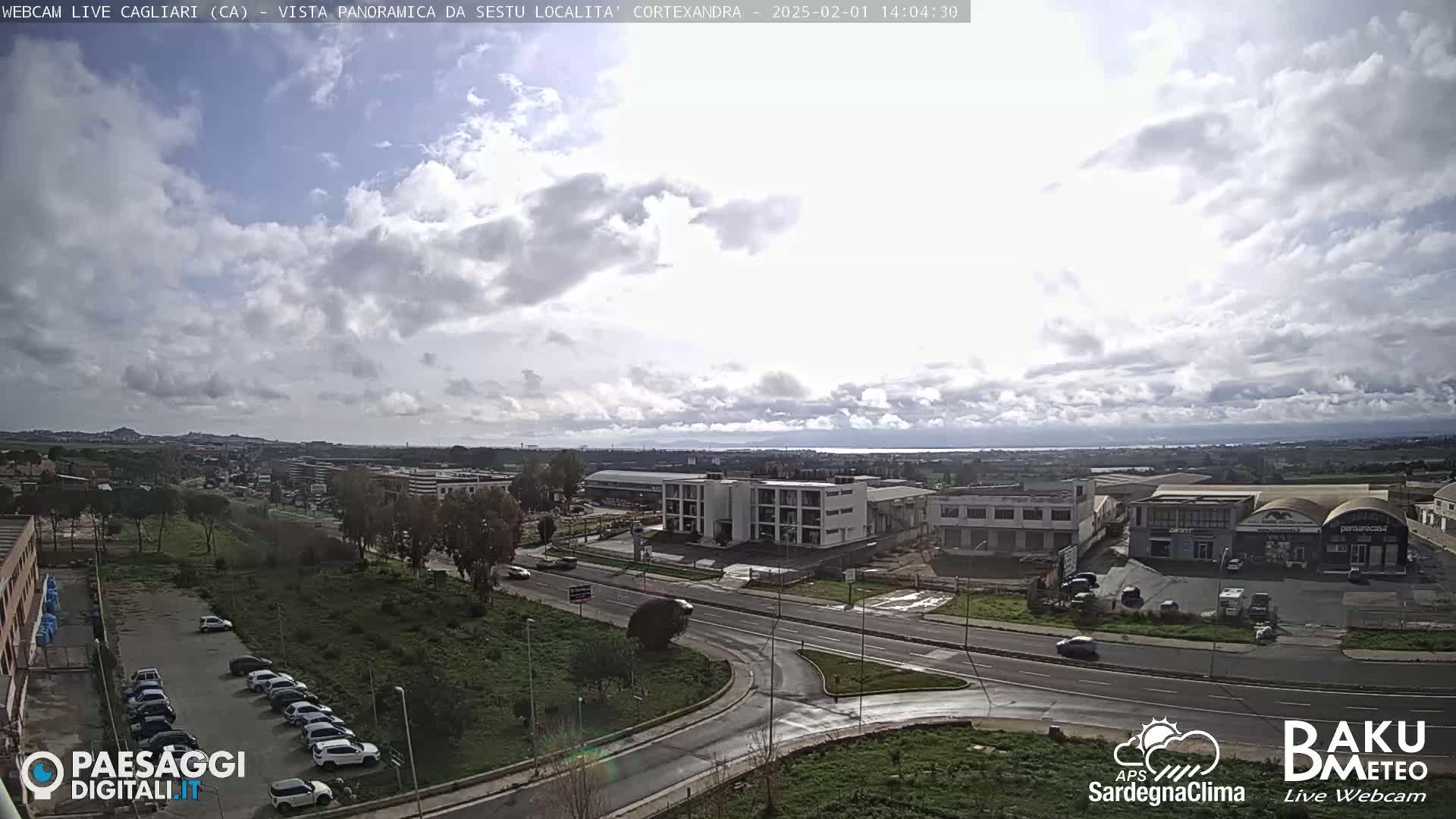 A partly cloudy day reveals a panoramic view of a city with industrial buildings and roads, and a parking lot with cars.
