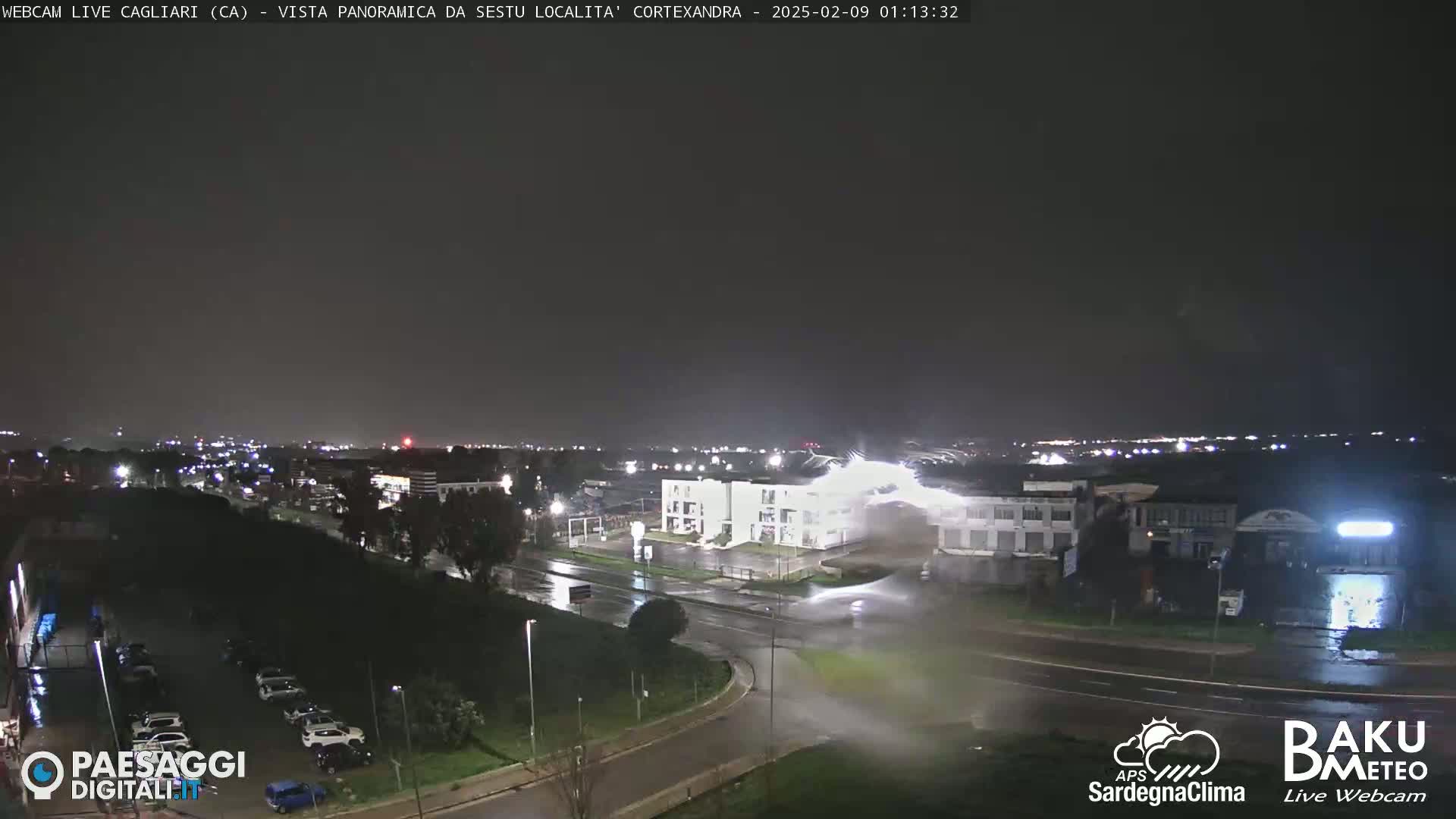 A nighttime view of a city intersection with heavy rain and lightning illuminating wet roads and buildings.