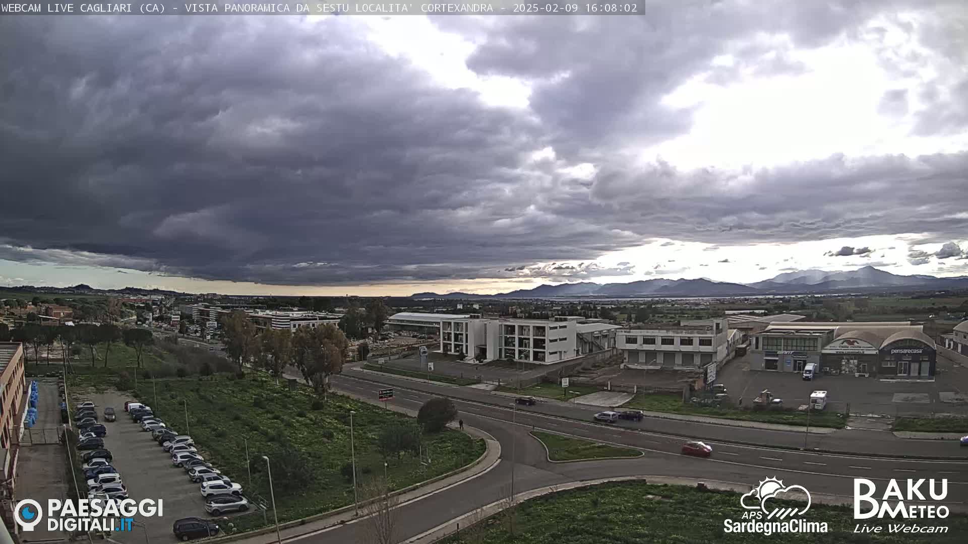 A panoramic view of a city under a mostly cloudy sky, with a distant mountain range visible on the horizon.