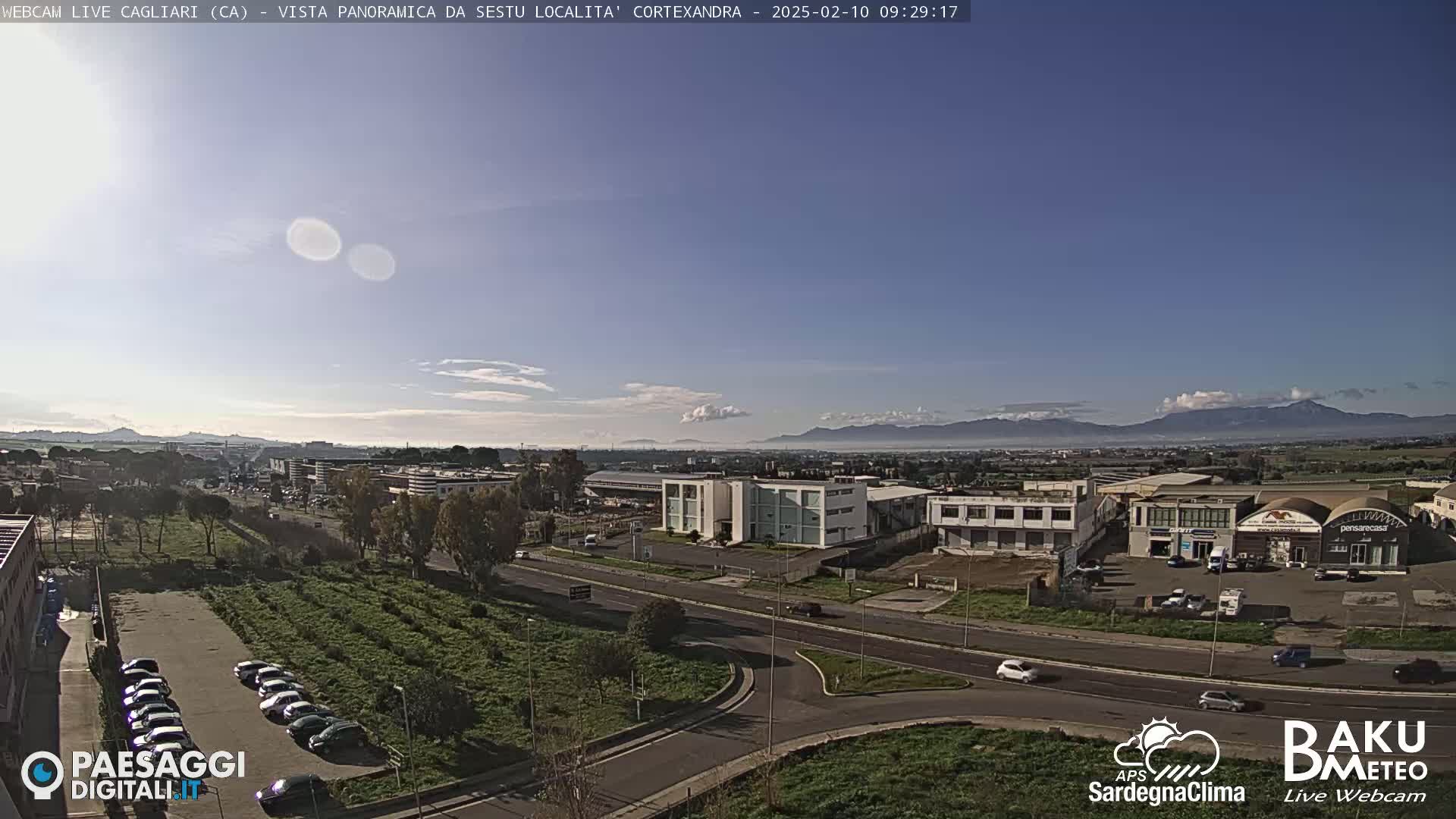 A clear, sunny day reveals a panoramic view of an industrial area and surrounding landscape, with mountains visible in the distance.