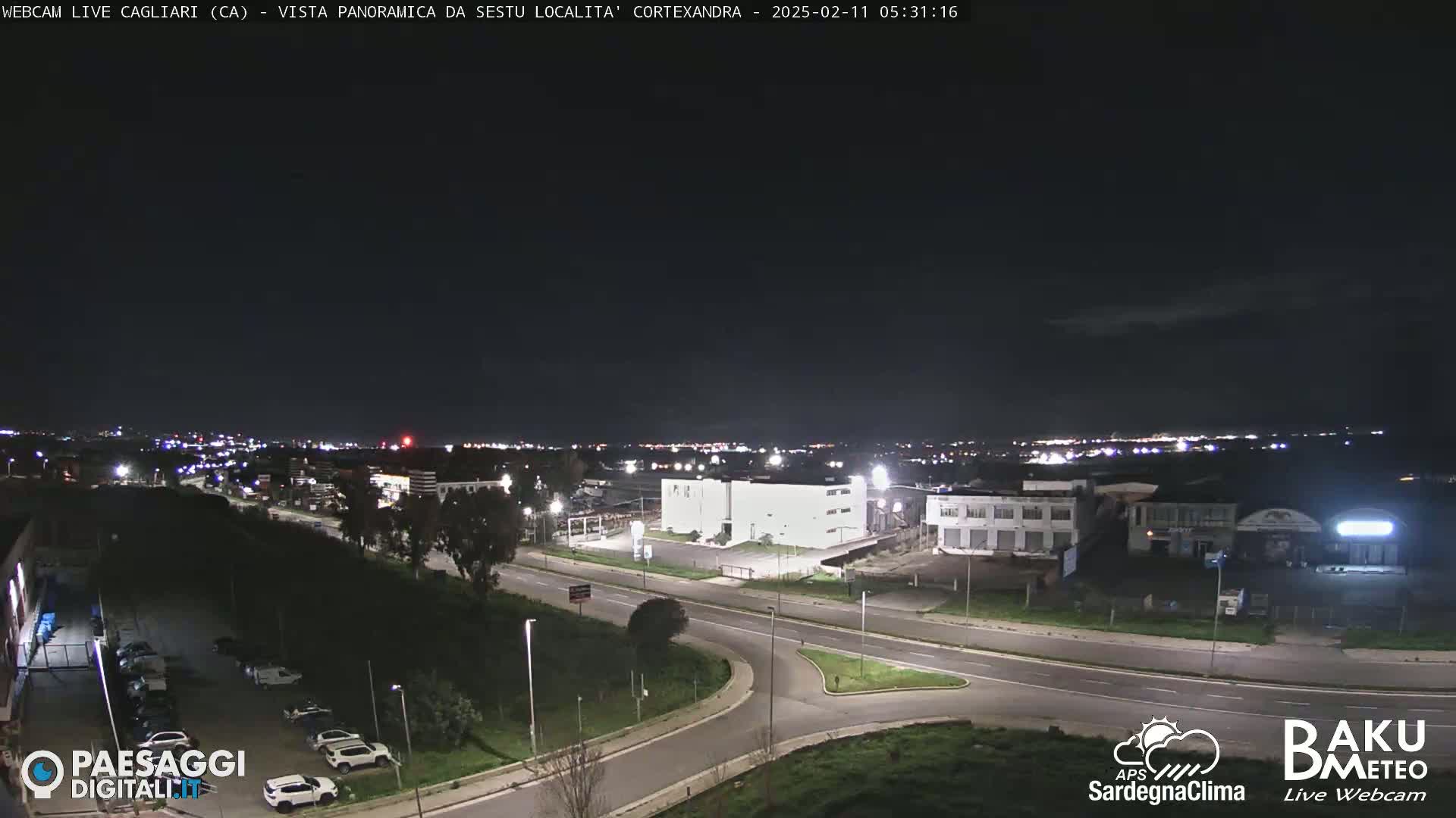 A nighttime, clear-sky view of a road intersection and surrounding industrial buildings in a city.