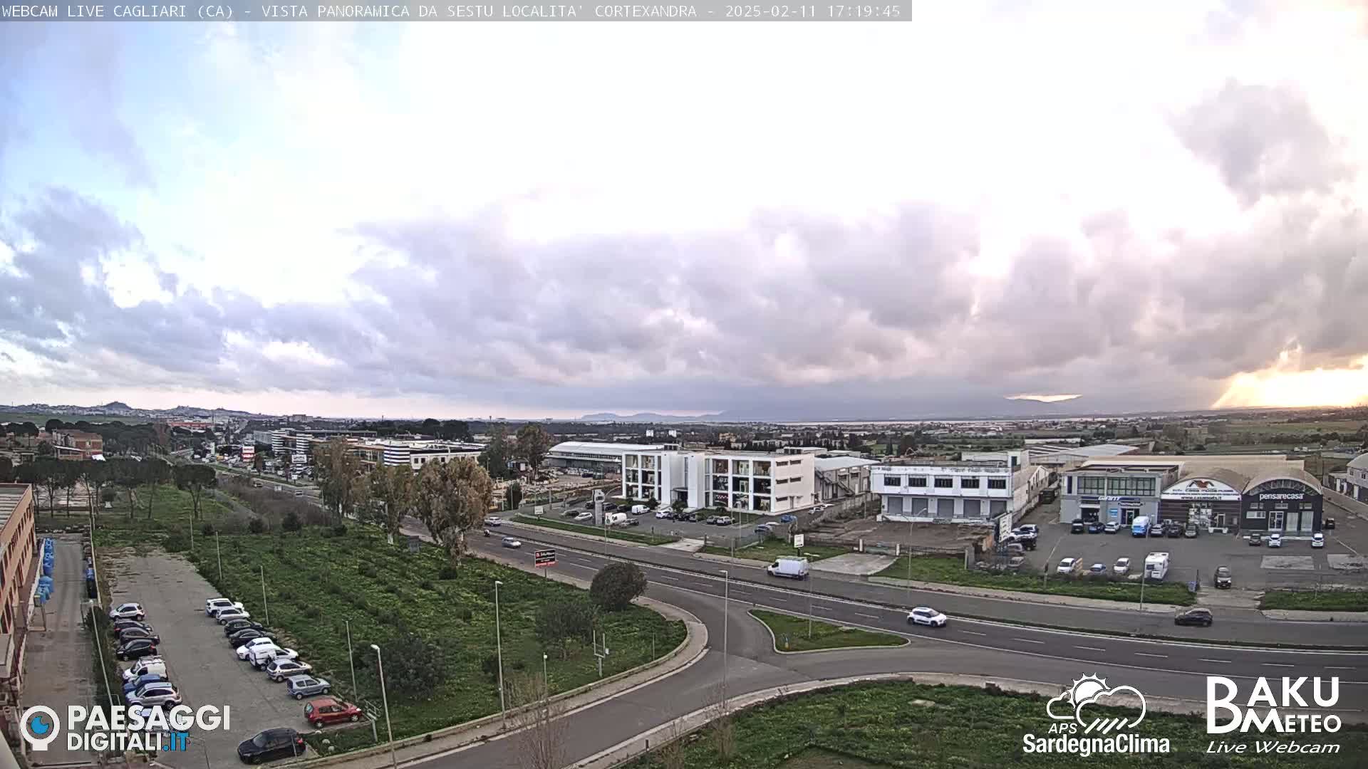 A mostly cloudy, overcast sky hangs over a sprawling industrial area and roadway, with distant mountains visible on the horizon.