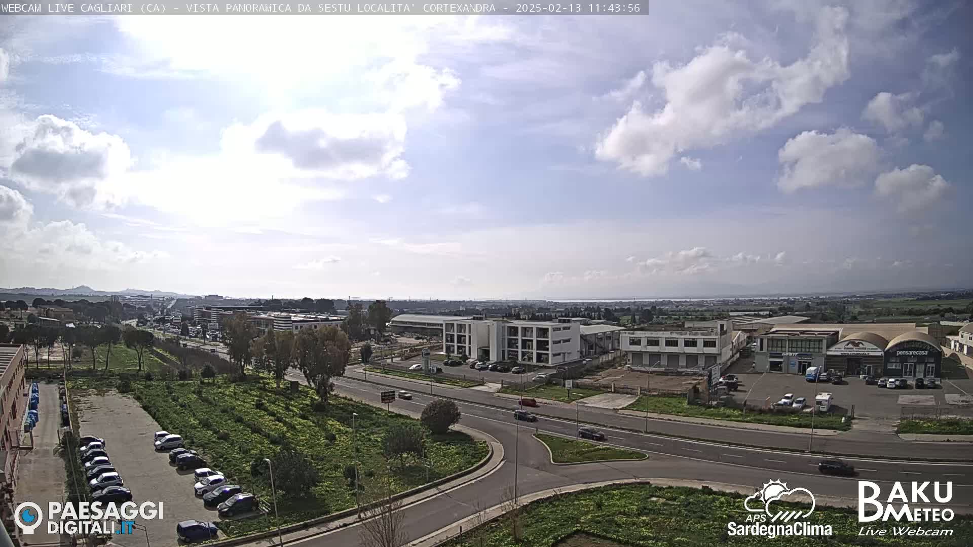 A partly cloudy day reveals a panoramic view of a city's industrial area and surrounding landscape, featuring roads, buildings, and parked cars.