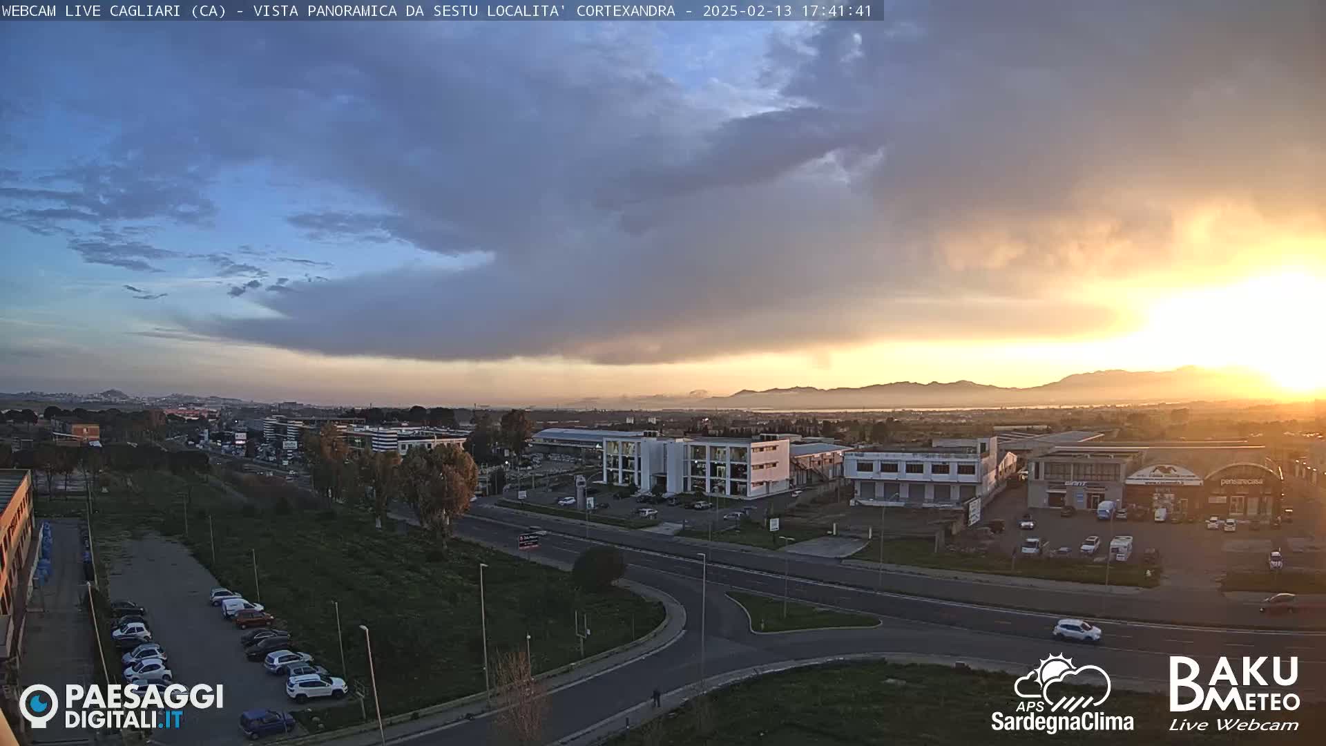 A sunset over a city, with partly cloudy skies and some haze or fog in the distance.