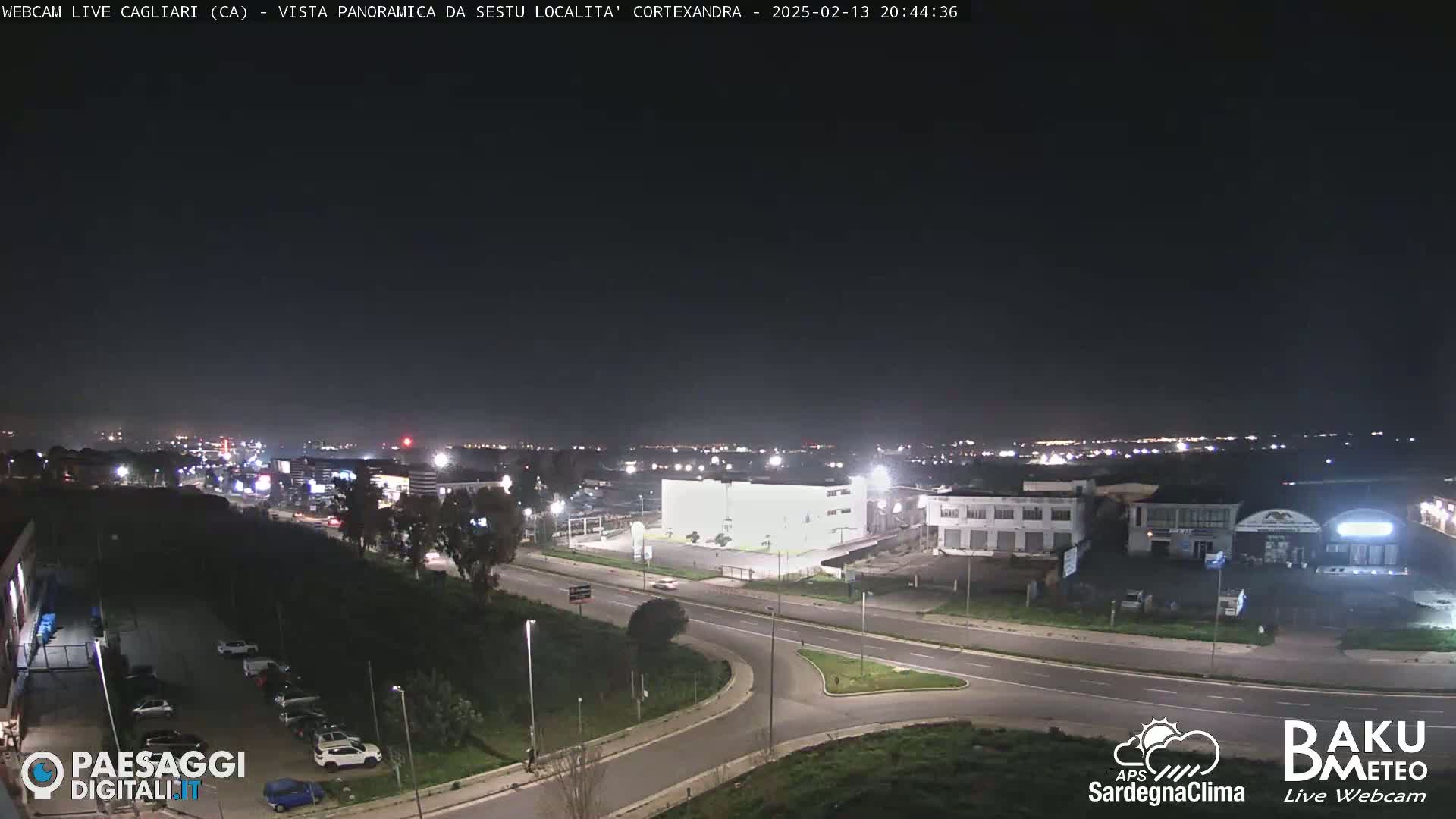 A nighttime, high-angle view shows a highway intersection and surrounding buildings and parking lots under a clear, dark sky.