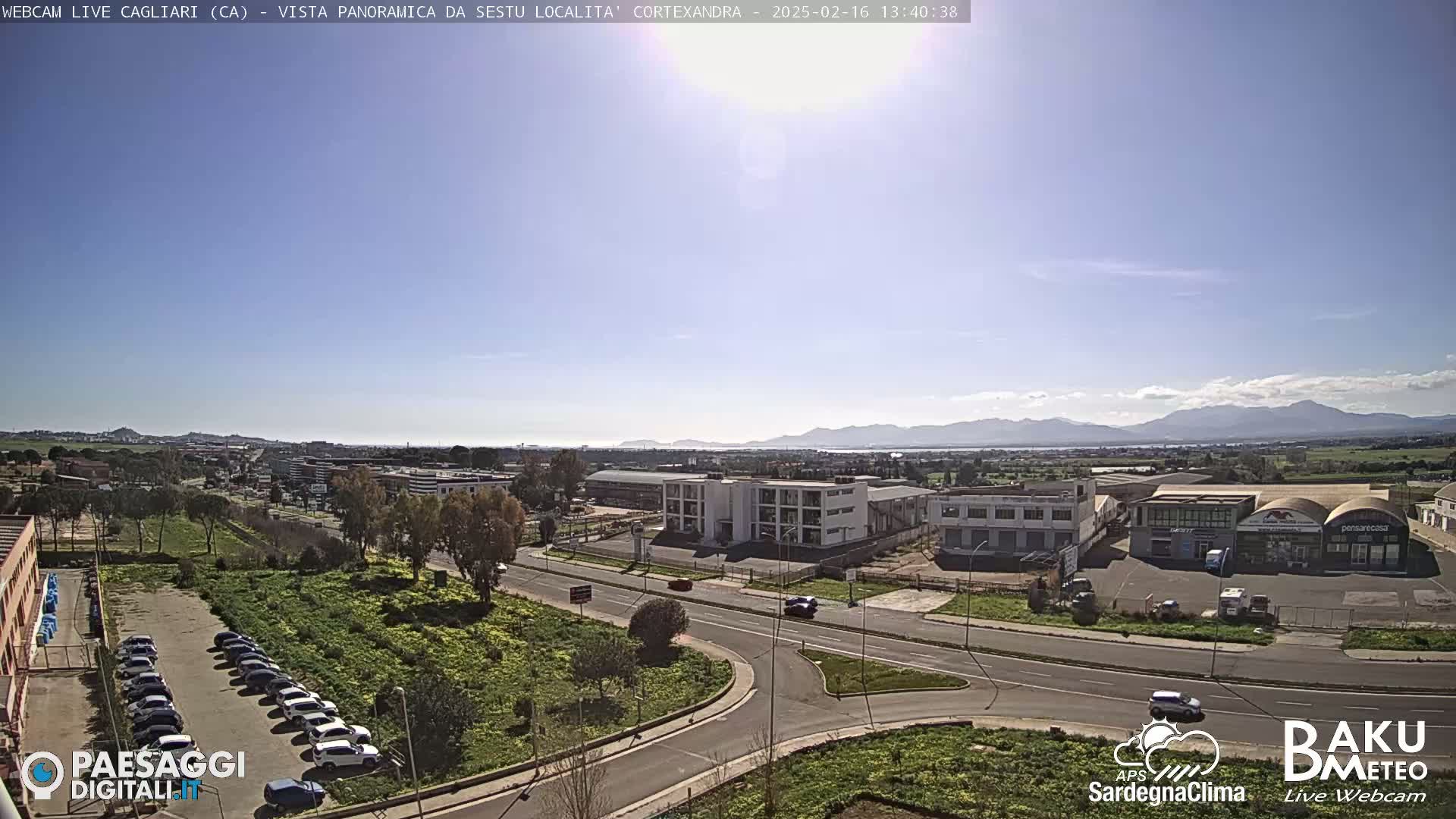A sunny day reveals a panoramic view of a city, featuring roads, buildings, parked cars, and distant mountains under a clear sky.