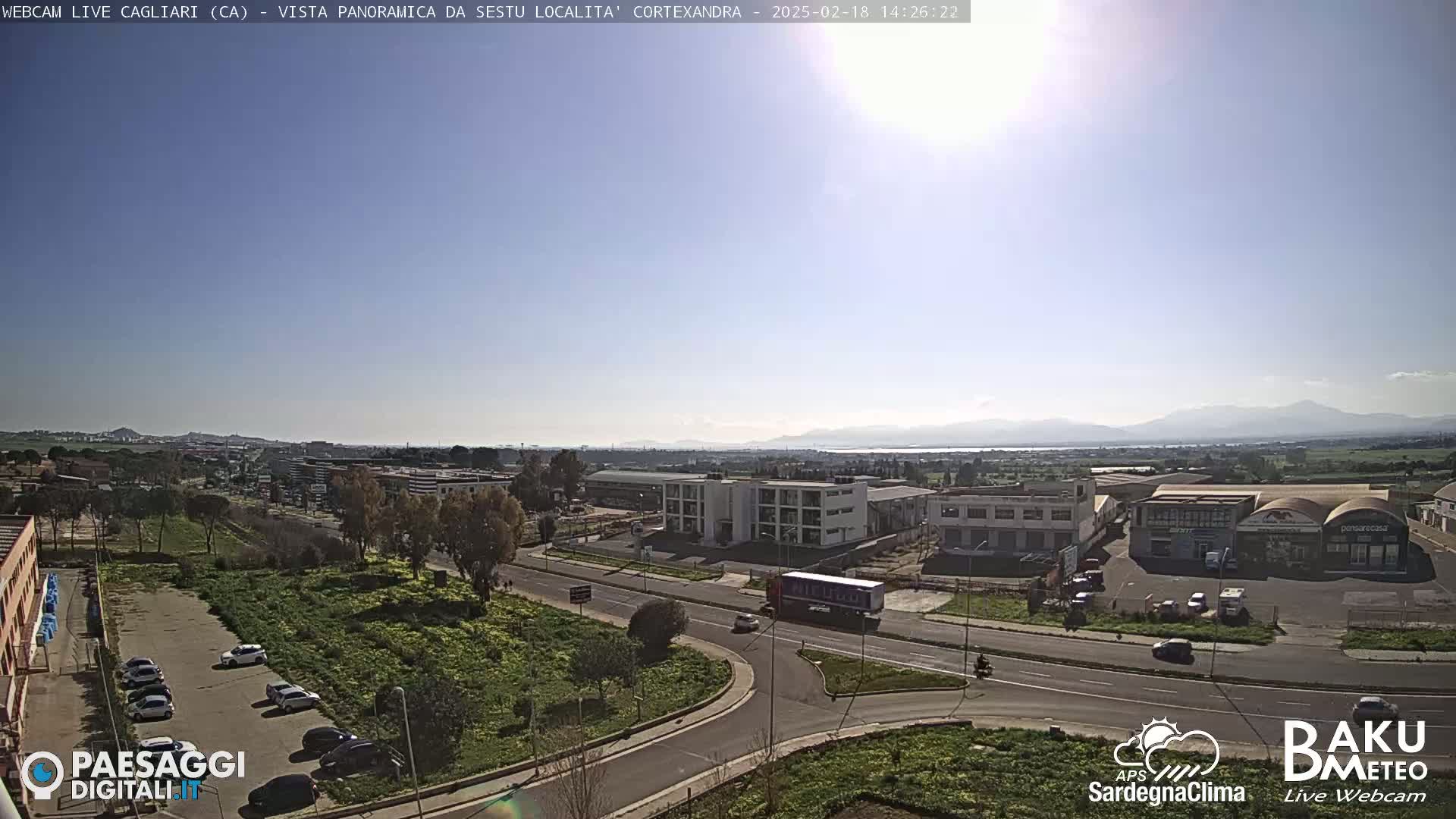 A sunny, clear day reveals a panoramic view of a suburban area with roads, buildings, and distant mountains.