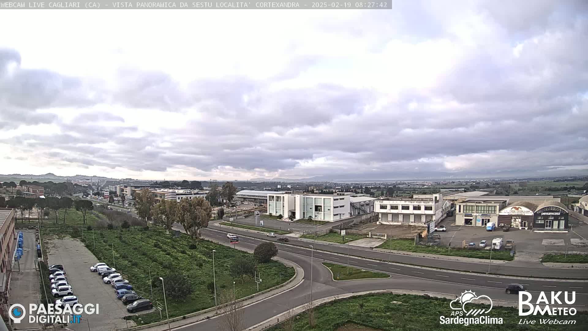A wide, slightly overcast view of a city with roads, buildings, and cars under a mostly cloudy sky.