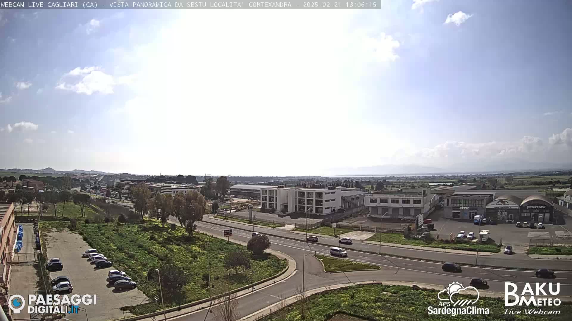 A partly sunny day reveals a panoramic view of an industrial area and surrounding roads with sparse traffic, near a body of water.