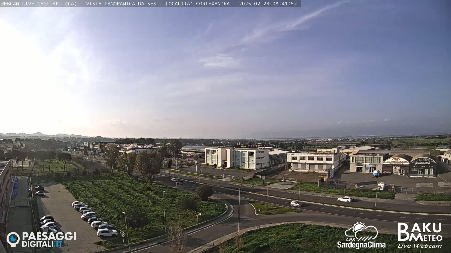 A mostly sunny, clear day overlooks a highway intersection and industrial area, with a few cars visible and distant hills in the background.