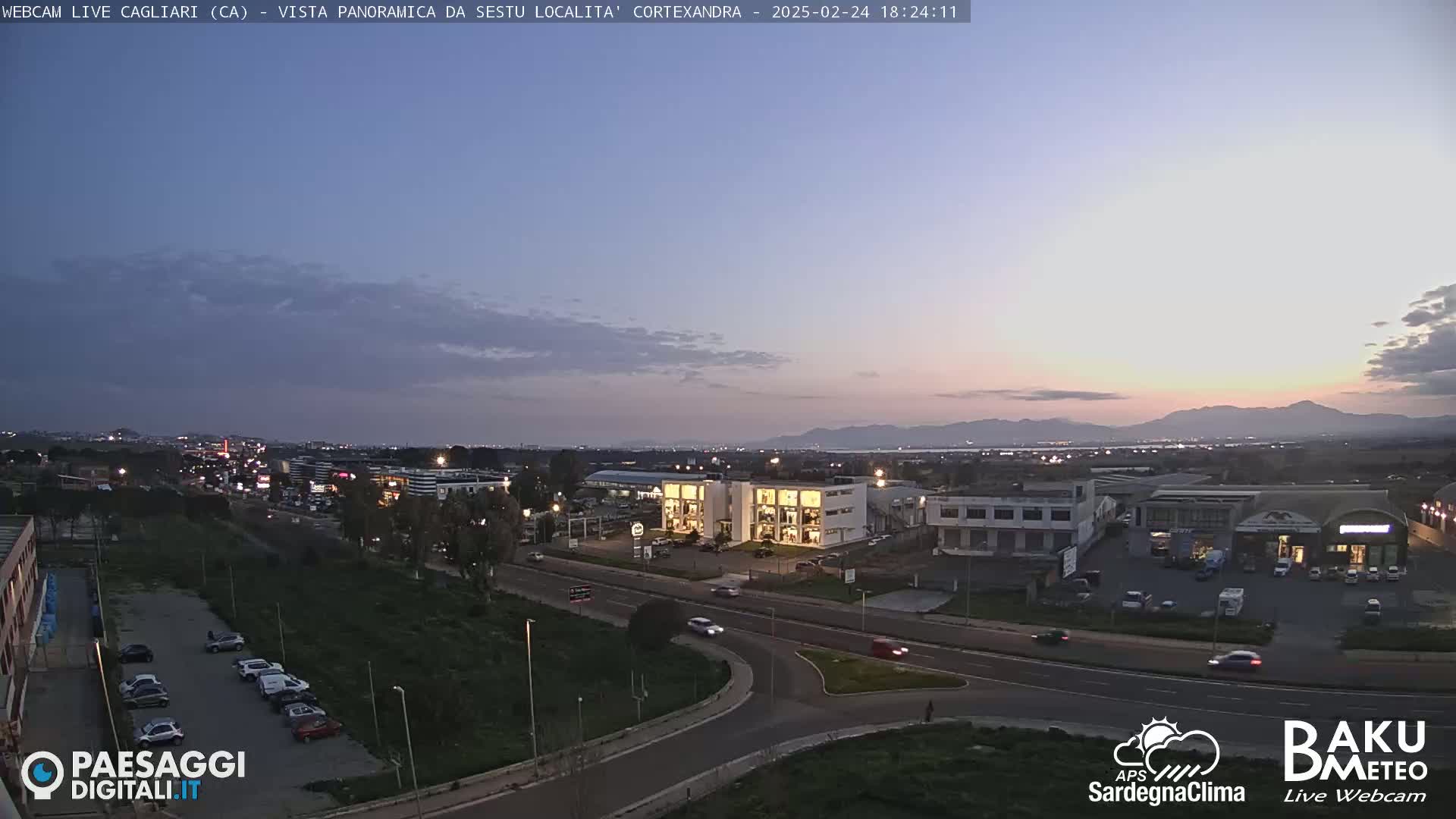 A twilight view of a city with a highway, buildings, and distant mountains under a mostly clear sky.