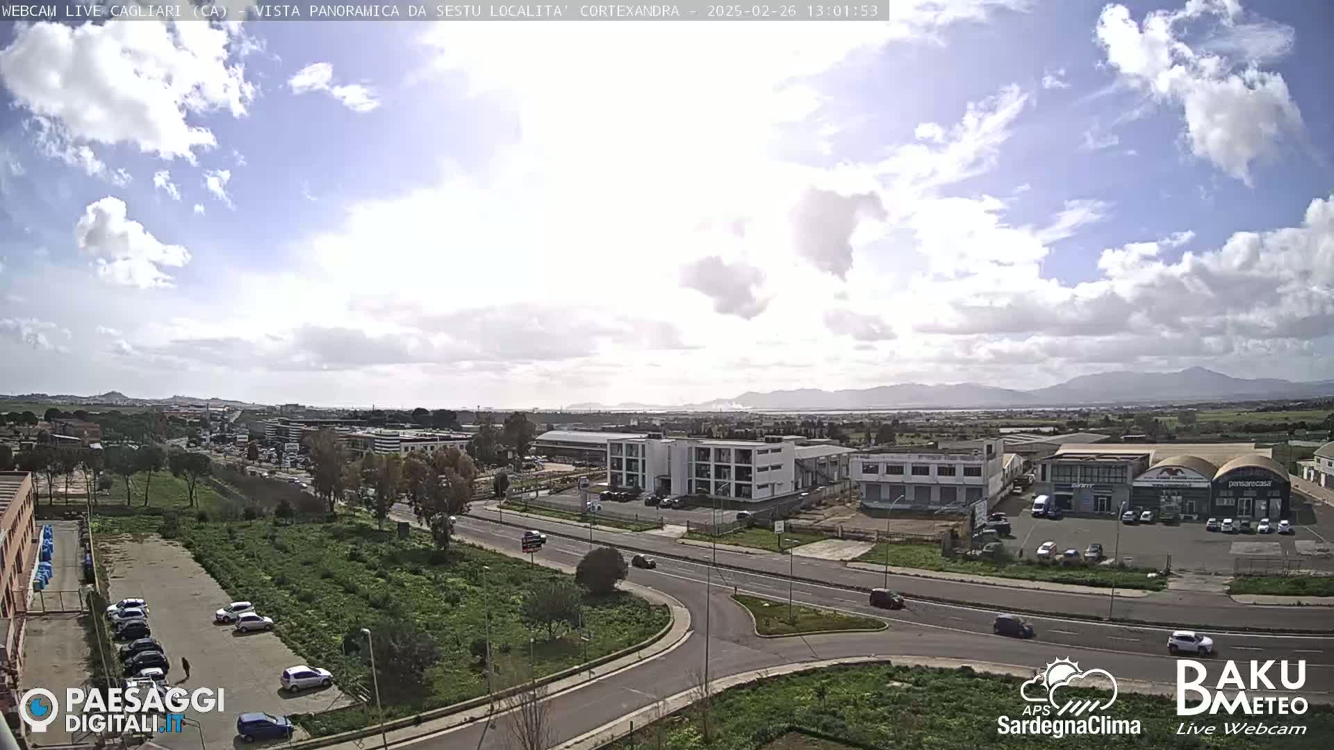 A partly cloudy daytime view of a highway intersection surrounded by industrial buildings and parking lots, with mountains visible in the distance.