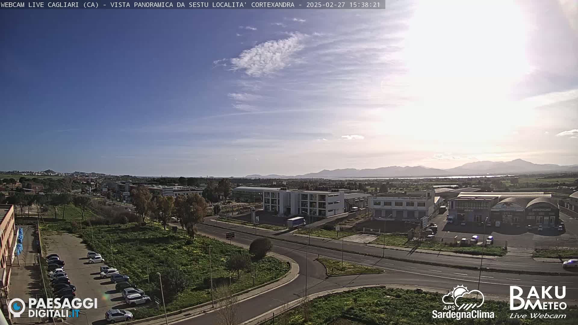 A mostly sunny day overlooks a city with a parking lot and roads, and distant mountains are visible in the background.