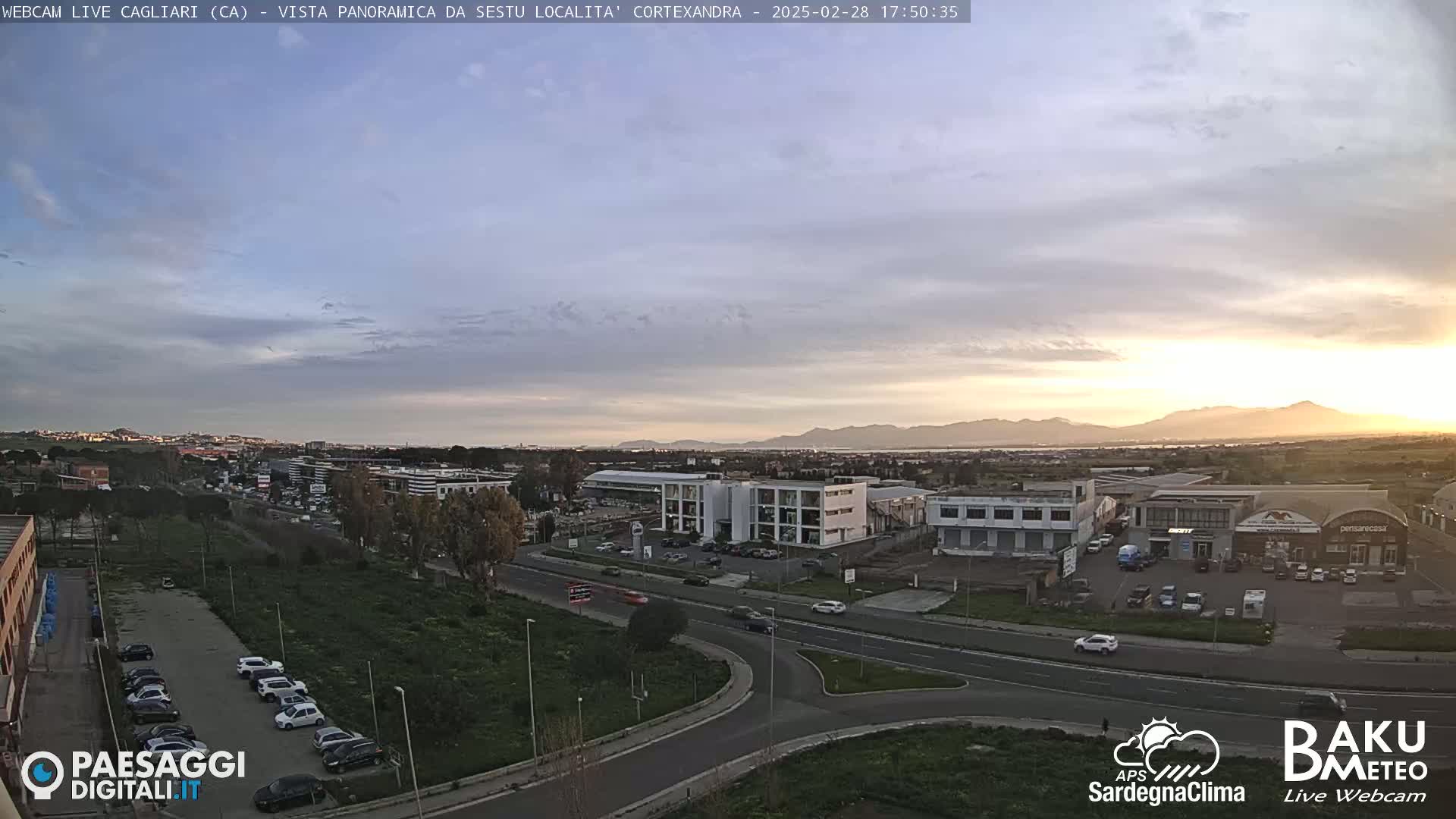 A mostly clear sunset over a cityscape and industrial area, with cars visible on roads and in parking lots.