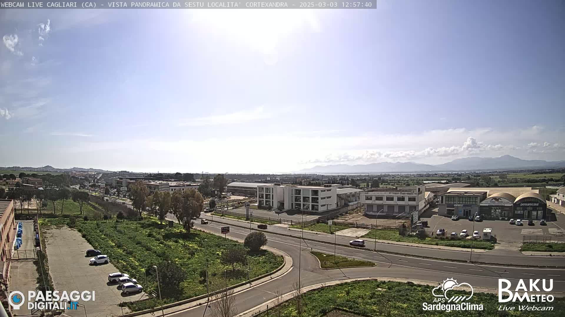 A panoramic view of a city under a mostly sunny sky with some scattered clouds and distant mountains in the background.