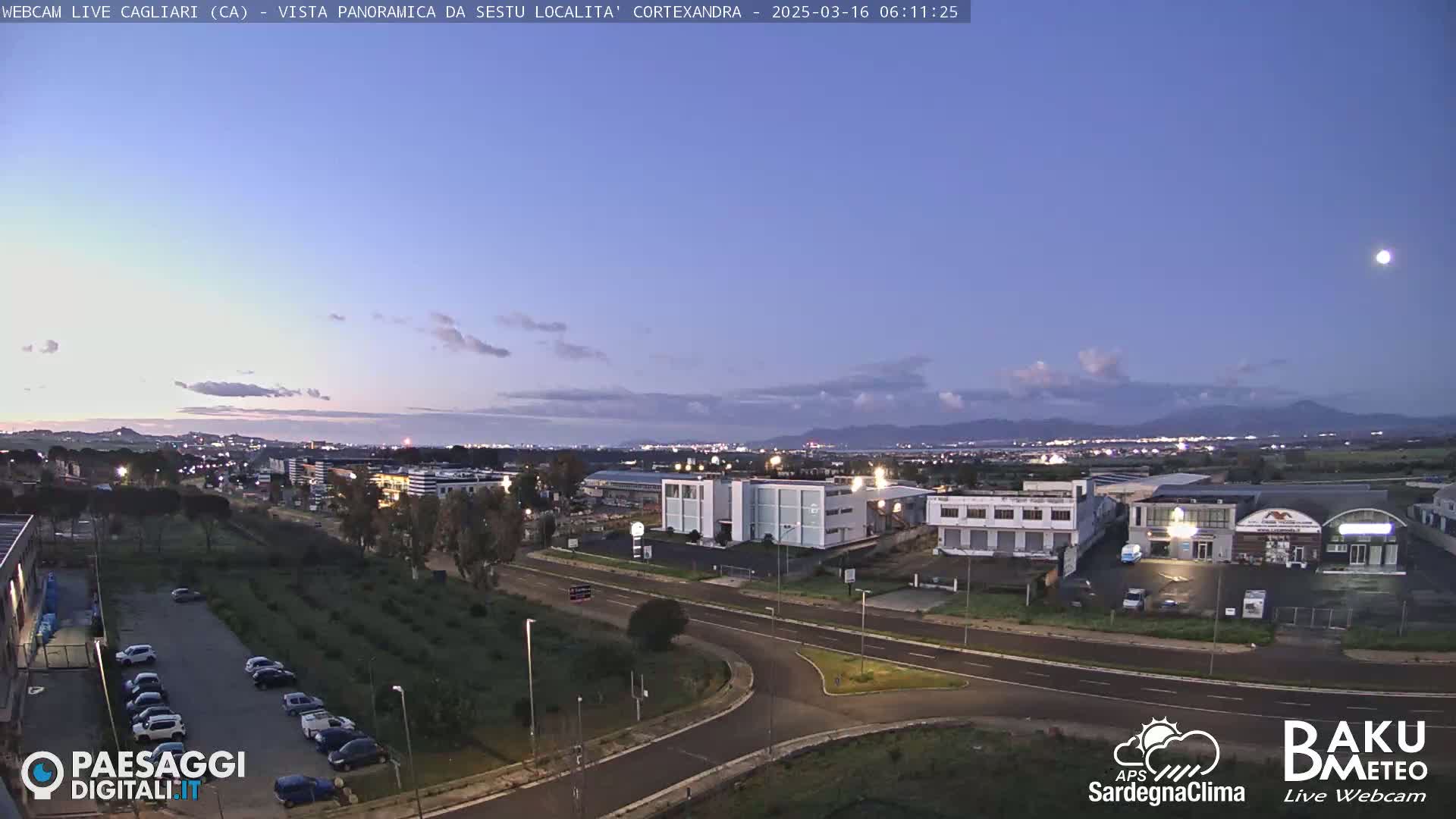 A twilight view of a city with industrial buildings and a parking lot, under a mostly clear sky.
