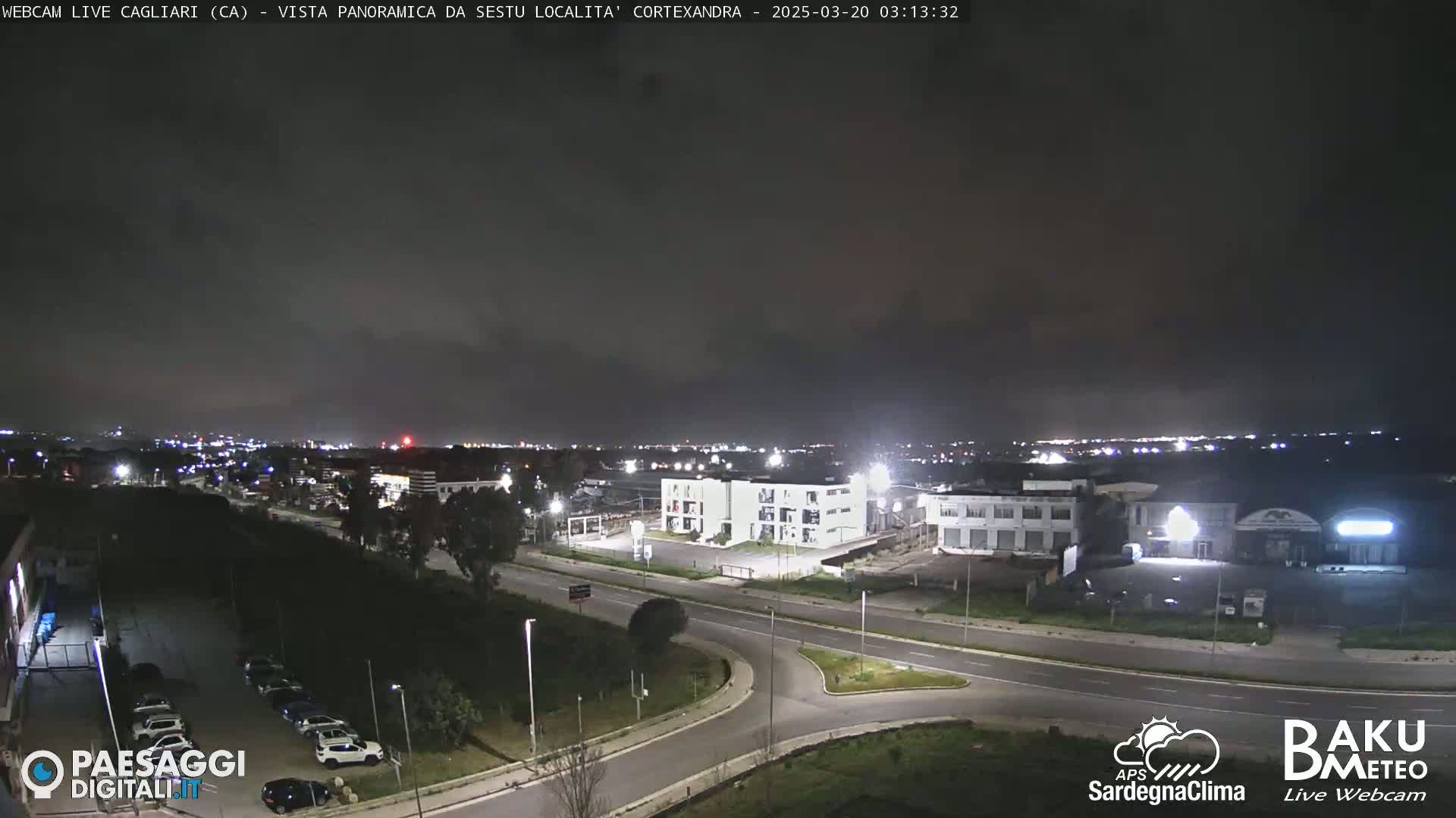 A nighttime, overcast view of a city with roads, buildings, and parked cars.