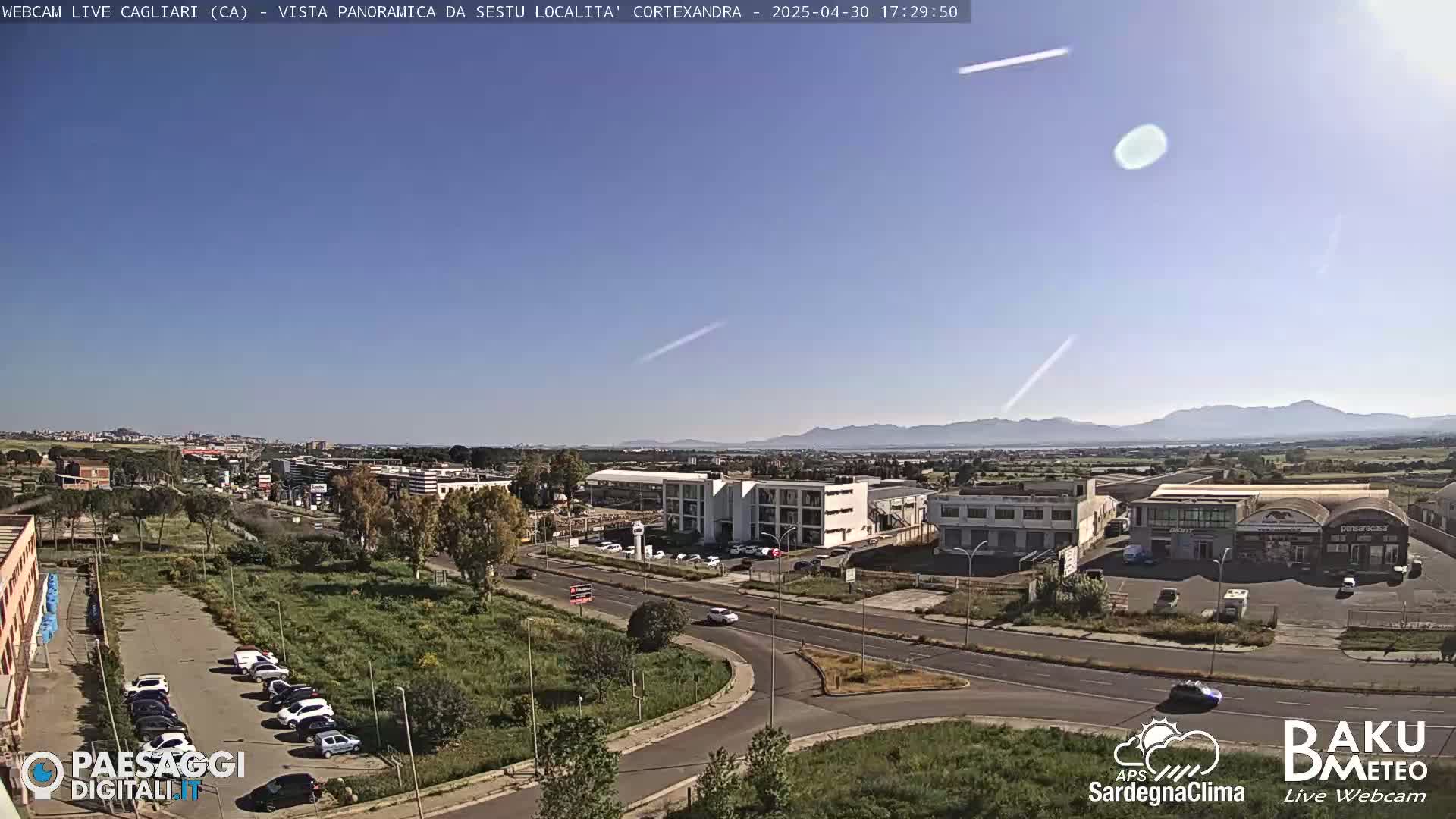 A high-angle, long shot on a clear, sunny day shows a parking lot and several buildings, roads, and distant mountains.
