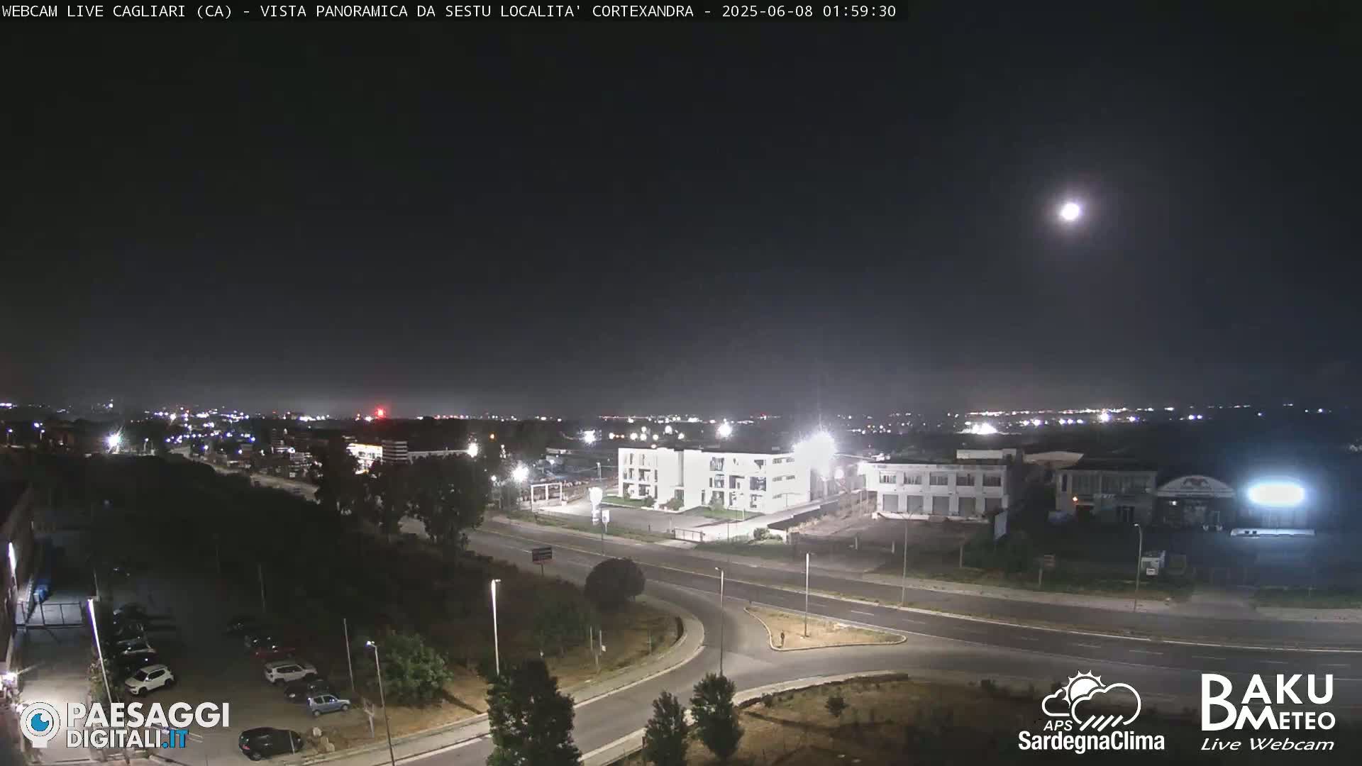 A nighttime, city view shows a highway intersection and surrounding buildings under a bright moon.