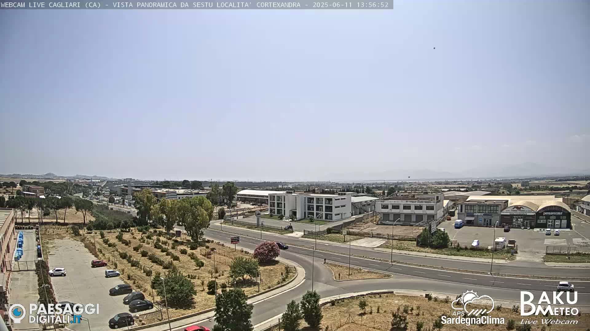 A panoramic view of a sunny industrial area and surrounding landscape, with roads and sparse vegetation visible.